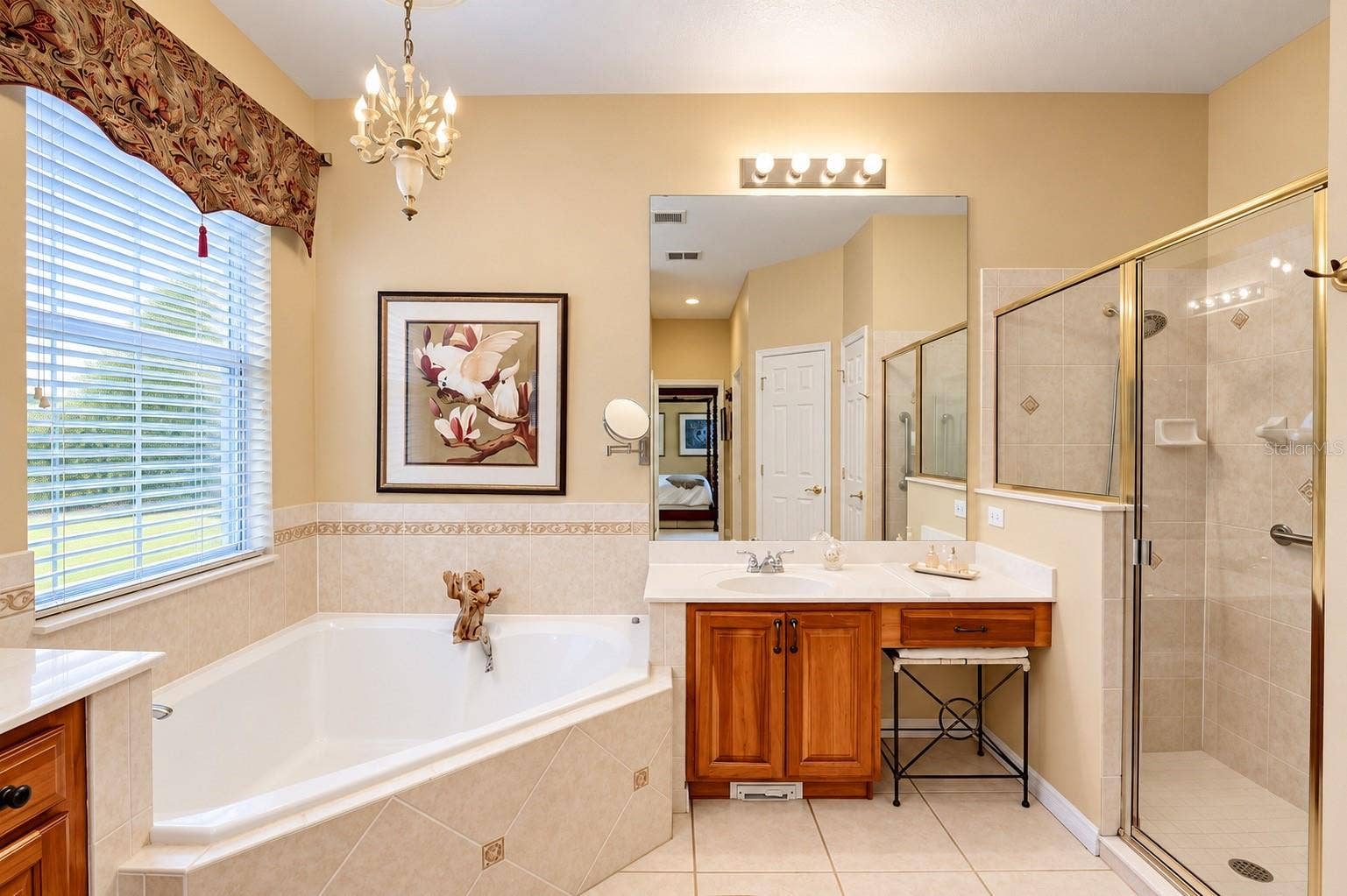 SPACIOUS AND ELEGANT PRIMARY BATHROOM FEATURING SOARING CEILINGS, A RELAXING OVERSIZED SOAKING TUB, AND A SEPARATE WALK-IN SHOWER WITH BEAUTIFUL CUSTOM TILEWORK AND GLASS ENCLOSURE! Enjoy DUAL VANITIES WITH BEAUTIFUL WOOD CABINETRY, GENEROUS COUNTER SPACE, AND ABUNDANT STORAGE! A large window fills the space with natural light, while elegant lighting and decorative tile accents add warmth and charm. THE PERFECT PRIVATE RETREAT TO RELAX AND UNWIND AFTER A LONG DAY!