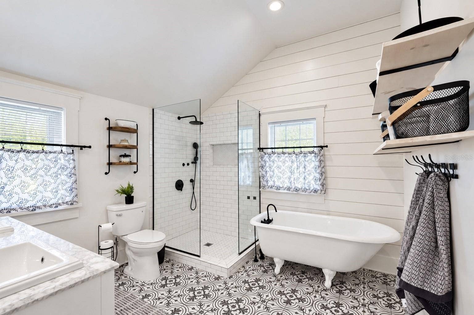 1901 10TH STREET, St Cloud, FL 34769 Beautifully updated upstairs bathroom conveniently located between both bedrooms, featuring a charming clawfoot soaking tub, spacious glass-enclosed walk-in shower, stylish patterned tile flooring, shiplap walls, and elegant black fixtures.