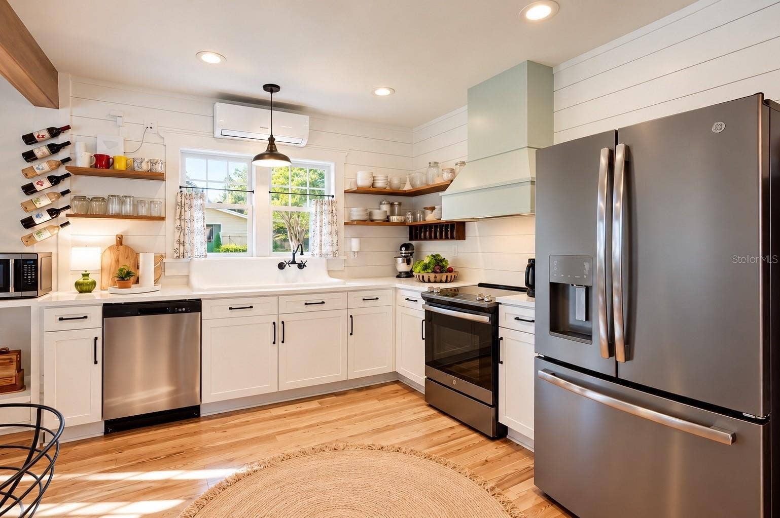 1901 10TH STREET, St Cloud, FL 34769 FARMHOUSE-STYLE KITCHEN featuring white shaker cabinetry, shiplap walls, floating wood shelves, gorgeous wood flooring, stainless steel appliances, and an OVERSIZED FARMHOUSE APRON-FRONT SINK with wall-mounted faucet beneath sun-filled windows overlooking the lush backyard, filled with an abundance of EDIBLE TREES, PLANTS, AND HERBS, offering a wonderful opportunity to embrace FARM-TO-TABLE LIVING RIGHT IN YOUR OWN BACKYARD!