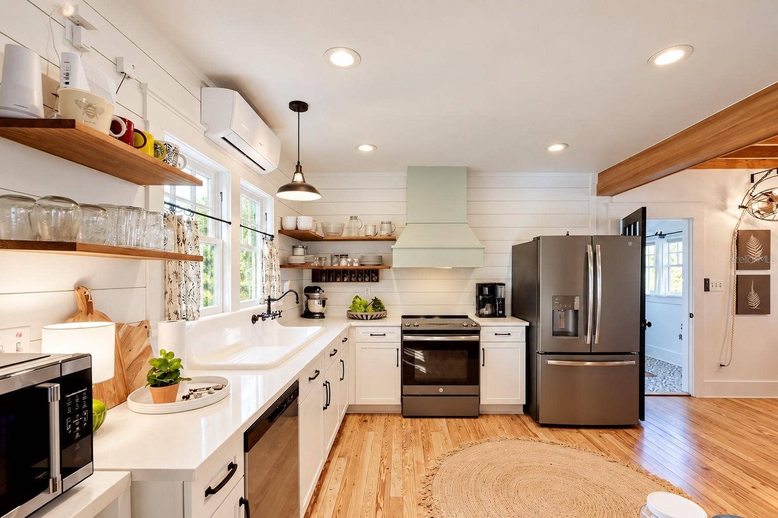 1901 10TH STREET, St Cloud, FL 34769 Updated FARMHOUSE-STYLE KITCHEN featuring white cabinetry, shiplap walls, gorgeous wood flooring, floating wood shelves, a charming OVERSIZED FARMHOUSE APRON-FRONT SINK beneath sun-filled windows, stainless steel appliances, and a stylish range hood!