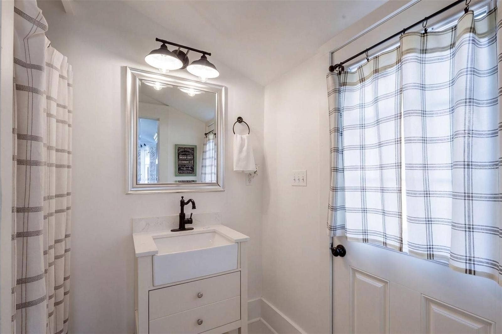 1901 10TH STREET, St Cloud, FL 34769 UPDATED FULL DOWNSTAIRS BATHROOM featuring a charming farmhouse-style vanity, stylish black fixtures, and modern lighting. Convenient exterior door provides direct access to the spacious FENCED BACKYARD AND BARN, perfect for enjoying the property's outdoor living spaces!