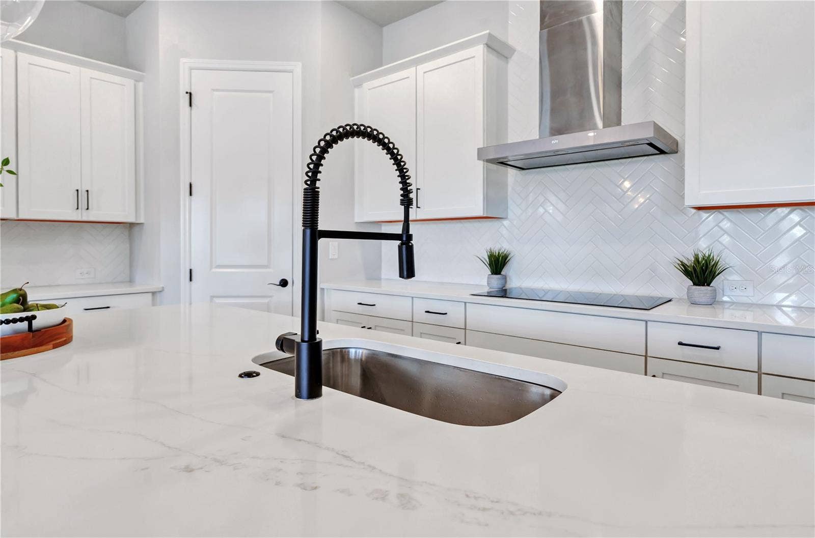 8336 CANETTI STREET, Orlando, FL 32827 Quartz counters, undermount sink, matte black faucet, and herringbone tile backsplash with a view into the home.