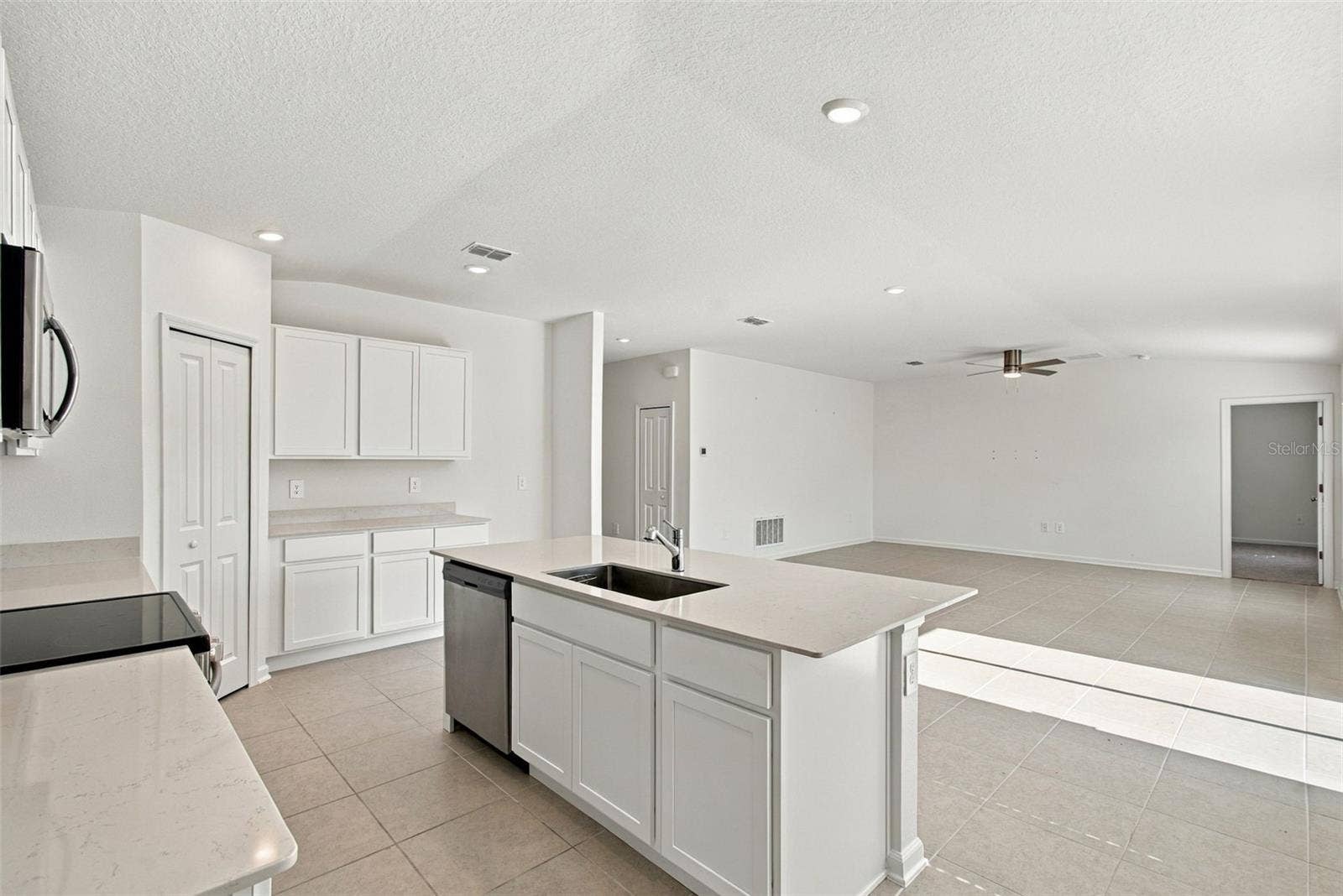 The kitchen offers a spacious island with breakfast bar, white Shaker-style cabinetry, and quartz countertops, all overlooking the dining and living areas.