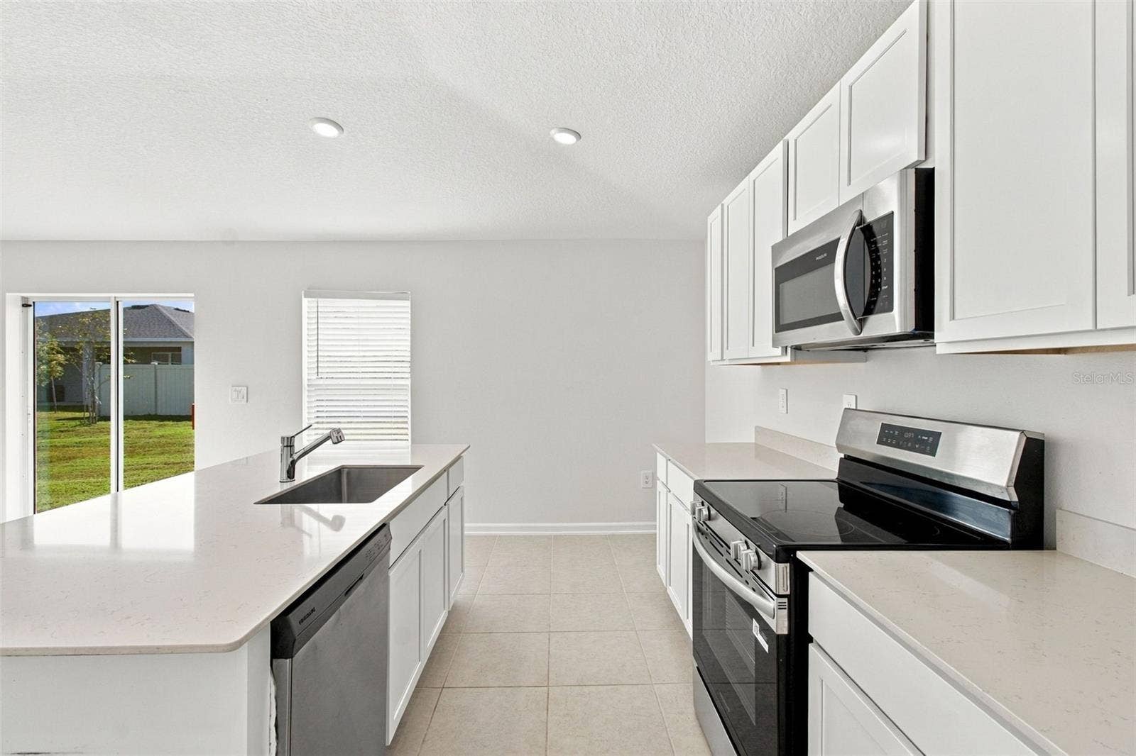 The kitchen offers a spacious island with breakfast bar, white Shaker-style cabinetry, and quartz countertops, all overlooking the dining and living areas.