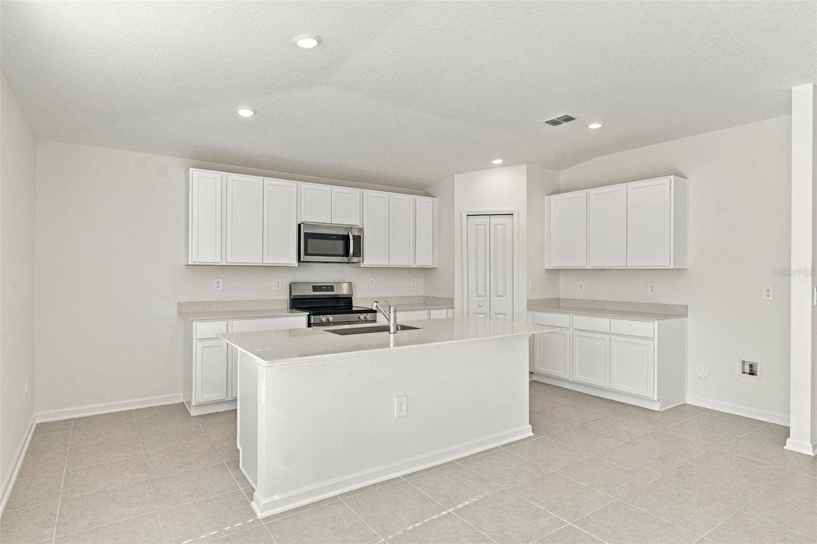 The kitchen offers a spacious island with breakfast bar, white Shaker-style cabinetry, and quartz countertops, all overlooking the dining and living areas.