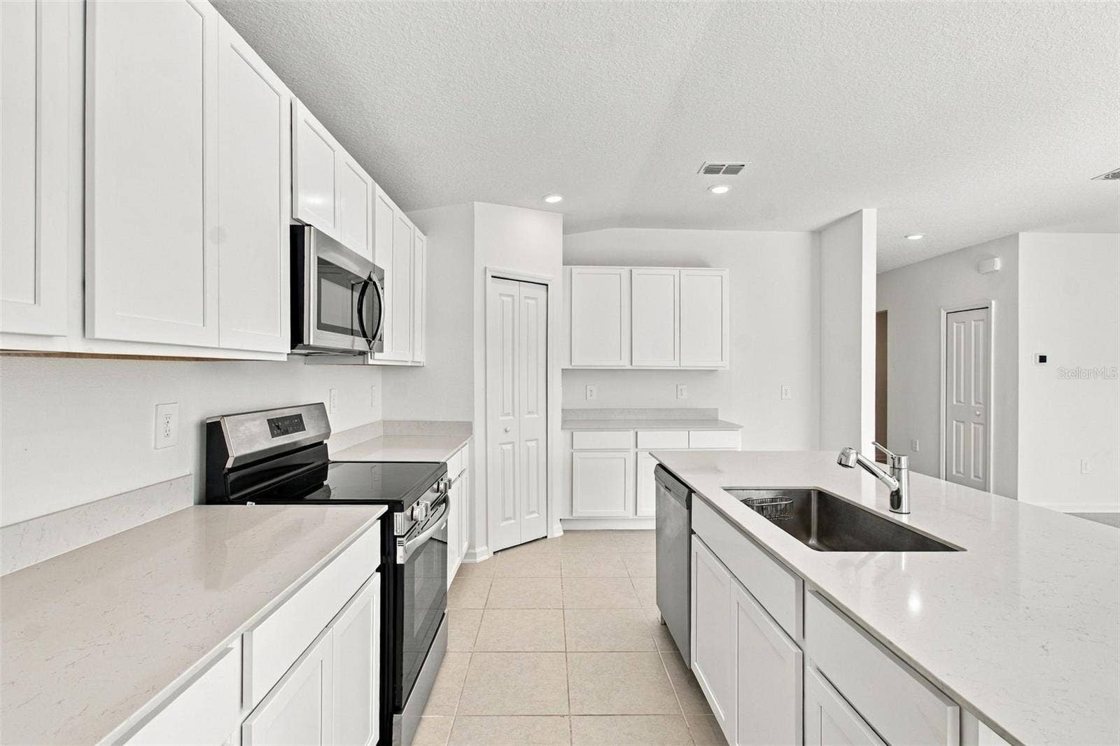 The kitchen offers a spacious island with breakfast bar, white Shaker-style cabinetry, and quartz countertops, all overlooking the dining and living areas.