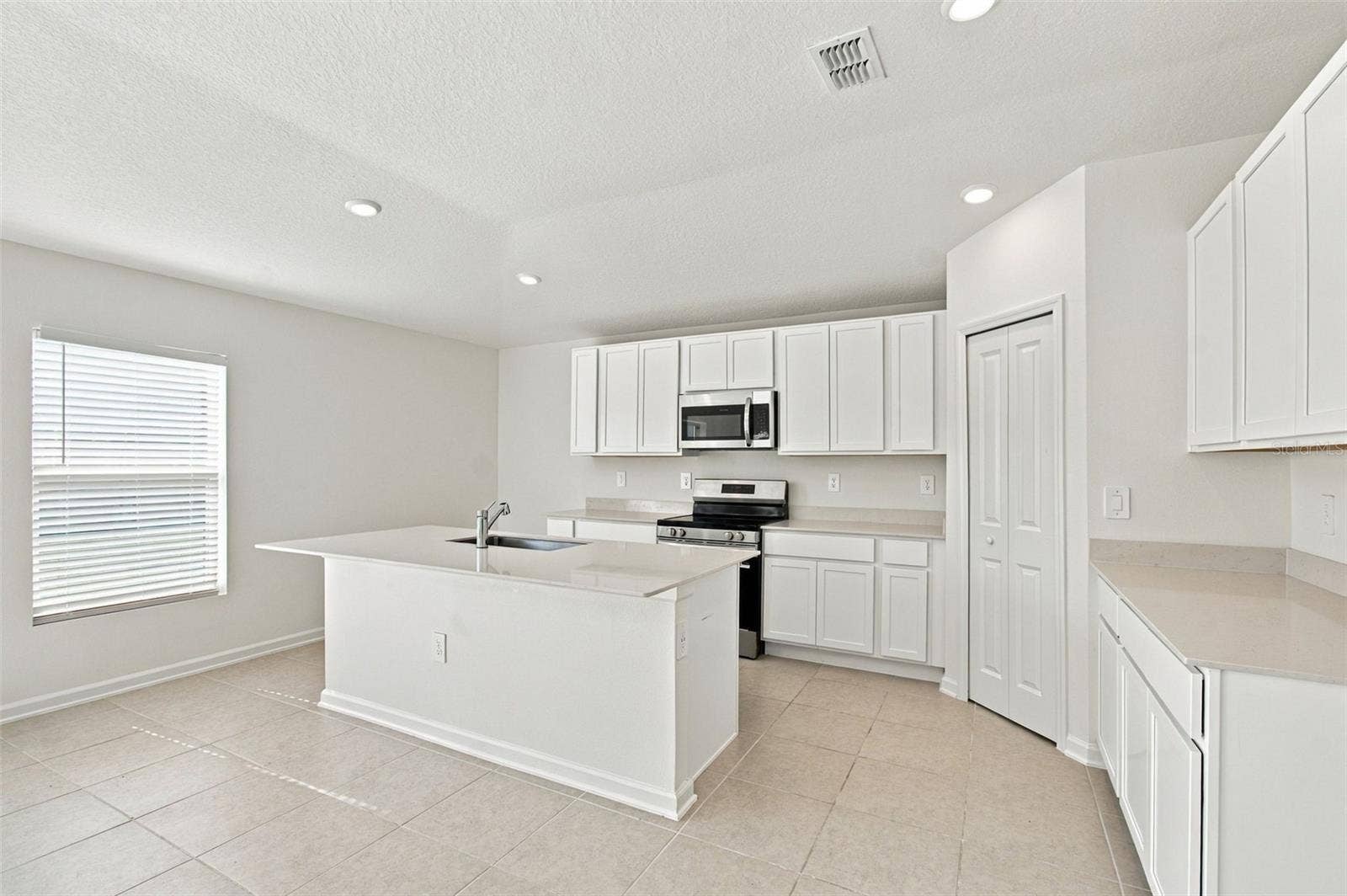 The kitchen offers a spacious island with breakfast bar, white Shaker-style cabinetry, and quartz countertops, all overlooking the dining and living areas.