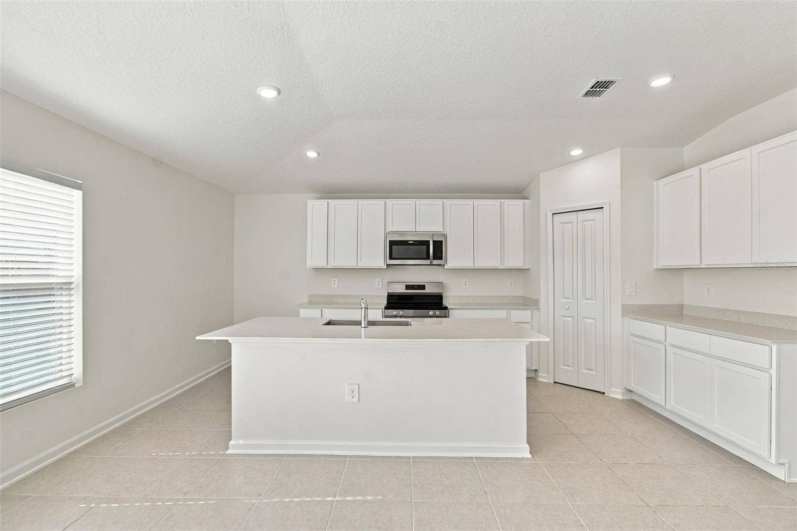 The kitchen offers a spacious island with breakfast bar, white Shaker-style cabinetry, and quartz countertops, all overlooking the dining and living areas.