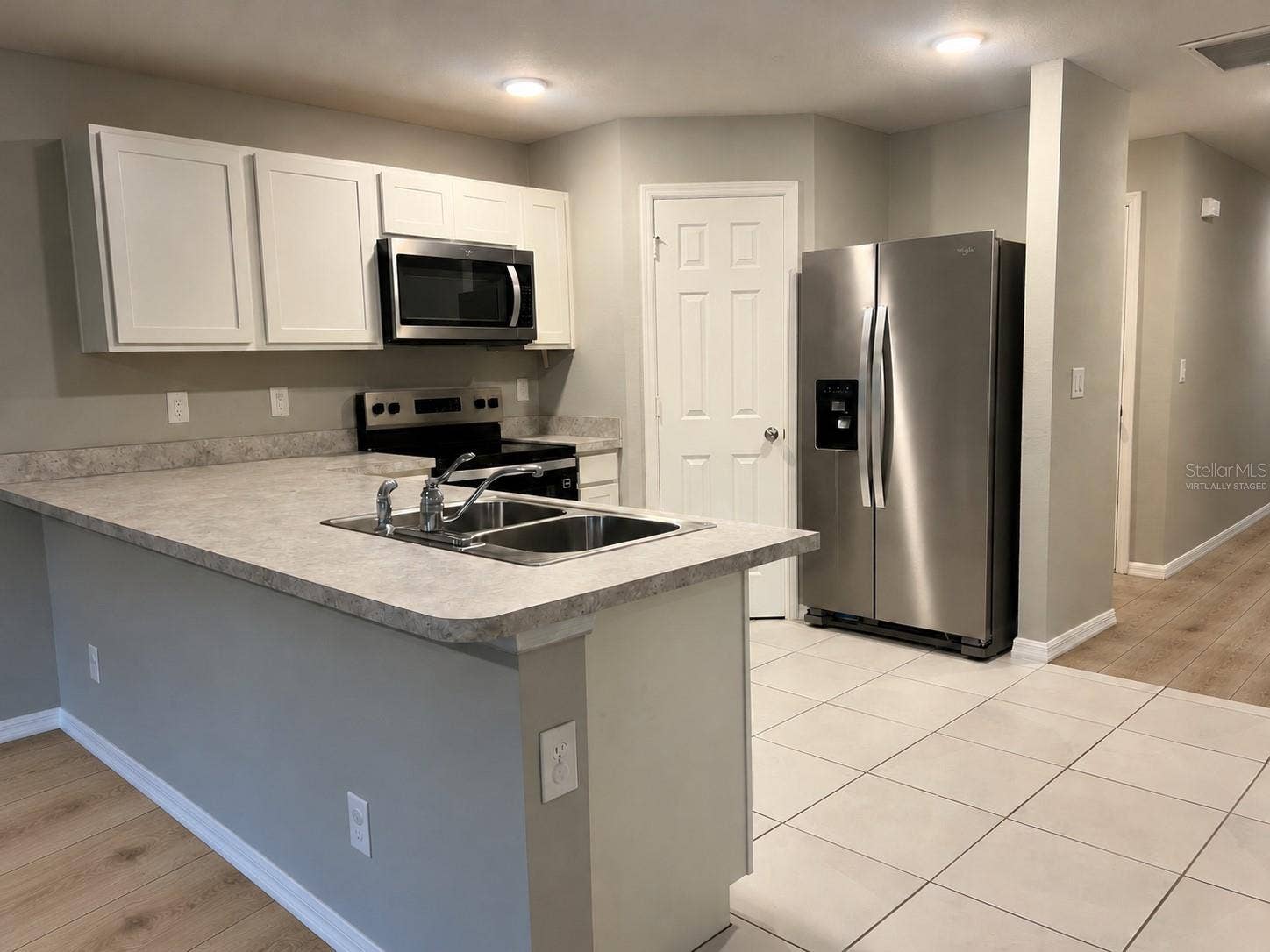 3404 61ST STREET W, Lehigh Acres, FL 33971 Kitchen peninsula virtually staged: planned laminate flooring in adjoining living area.