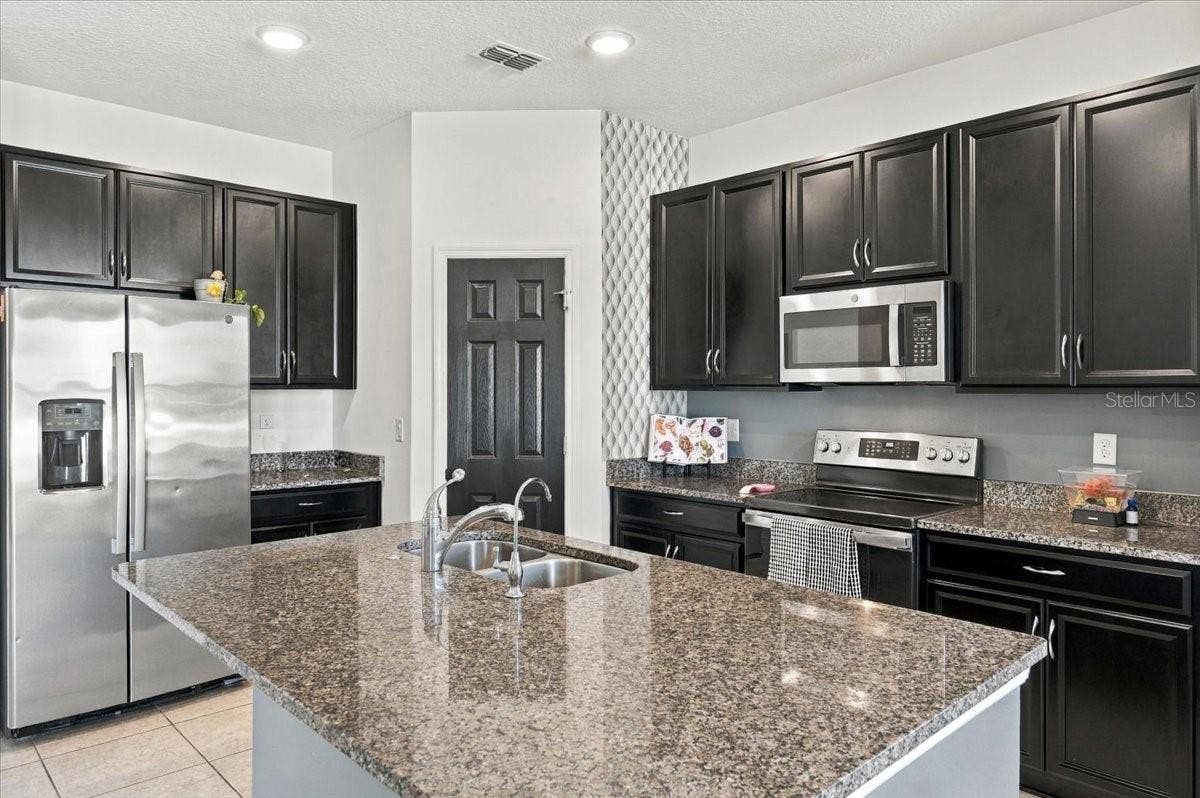 Spacious kitchen featuring granite countertops, dark cabinetry, stainless steel appliances, and a large center island.