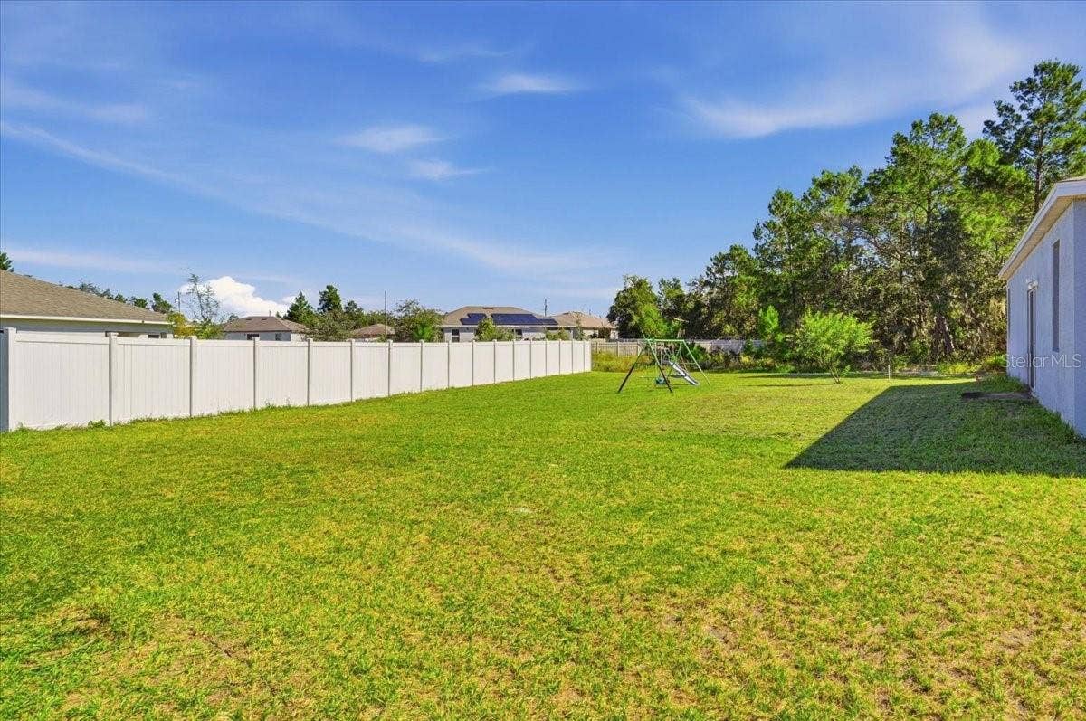 Expansive backyard featuring a large grassy area and white privacy fencing along one side of the property.