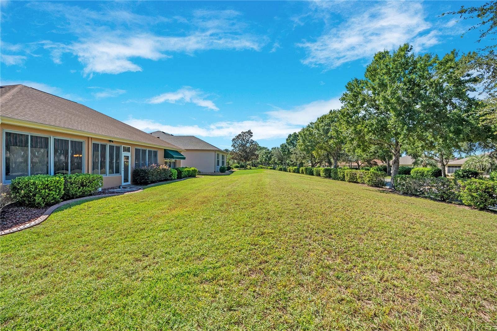 Expansive grassy backyard offers an inviting outdoor setting with mature trees and