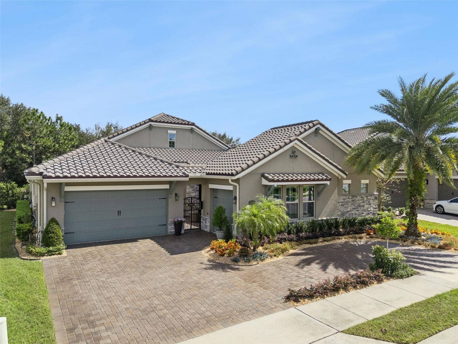 Elegant, Mediterranean-inspired exterior w/ tile roof, paver driveway, lush tropical landscaping and a gated courtyard entrance
