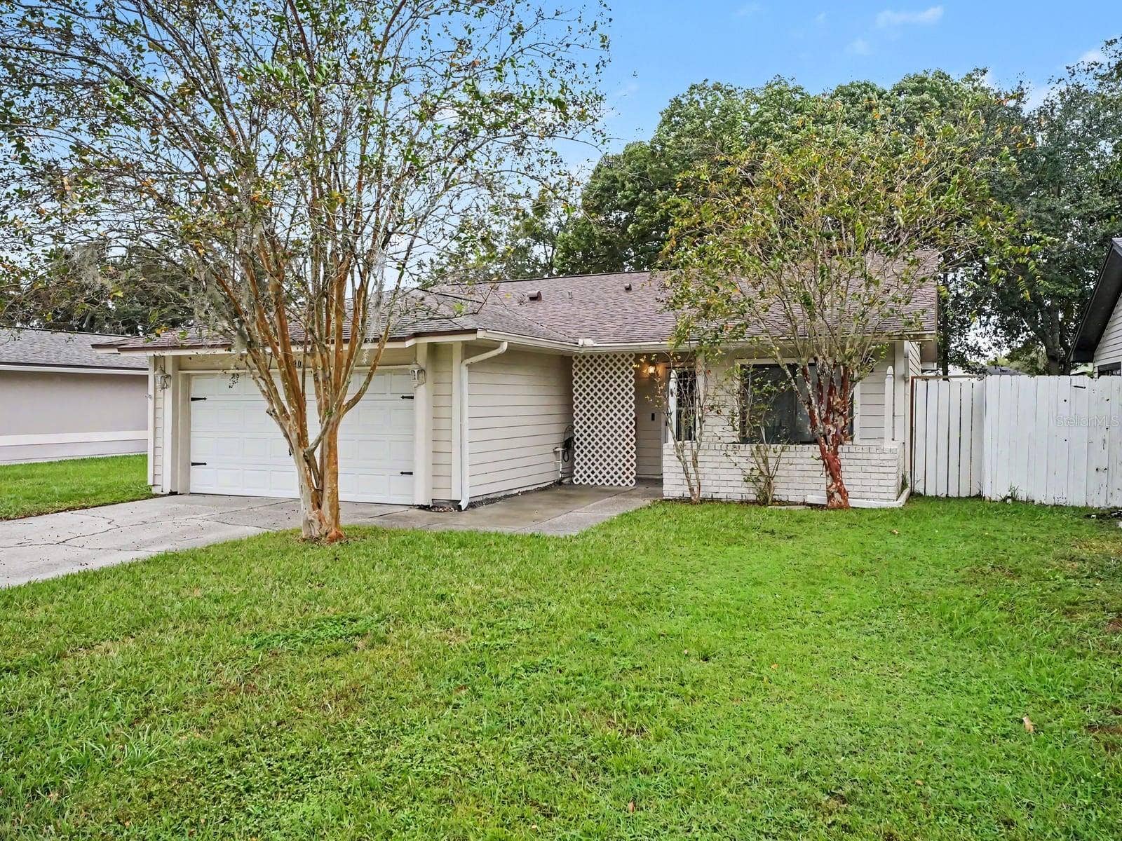 Welcoming entrance flanked by mature trees & white fencing