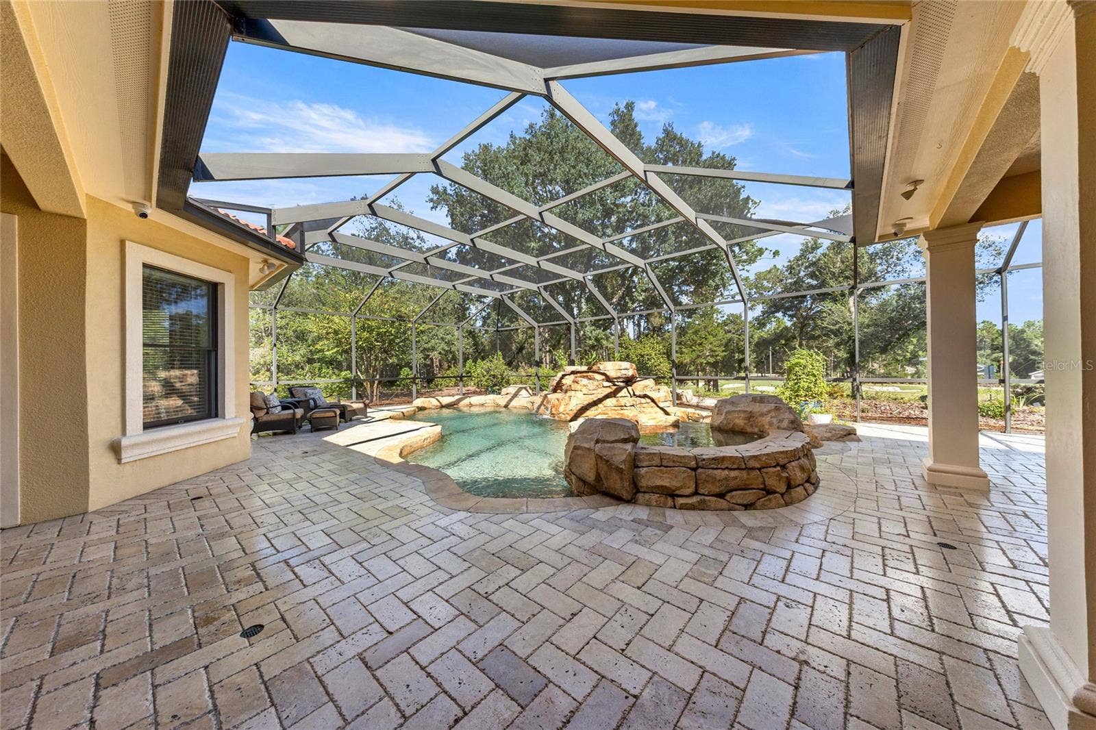 Resort-style outdoor retreat featuring a custom pool, raised spa, screened enclosure, and covered entertaining area.