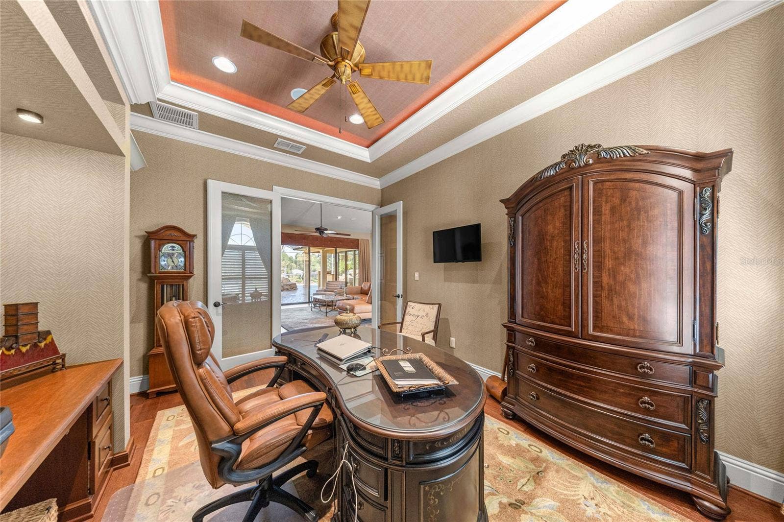 Private office or media room featuring a stunning illuminated tray ceiling, custom built-ins, and rich wood flooring.