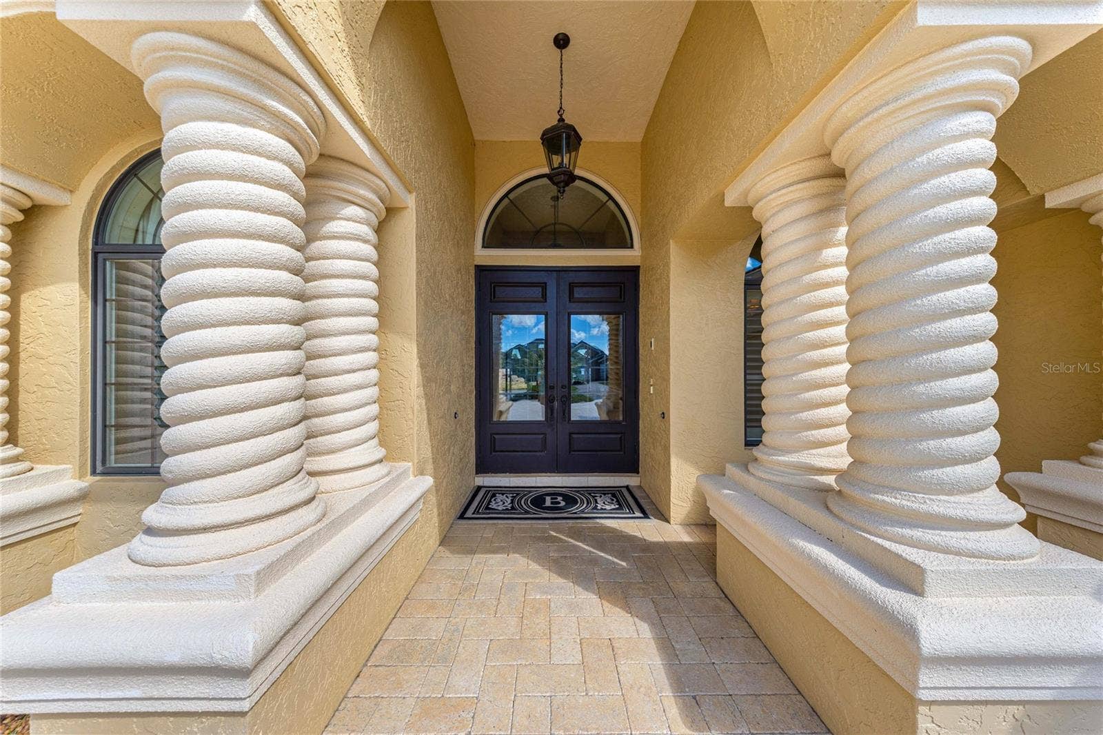 Impressive covered entryway featuring distinctive spiral columns, decorative arches, elegant double doors, and beautiful paver flooring.