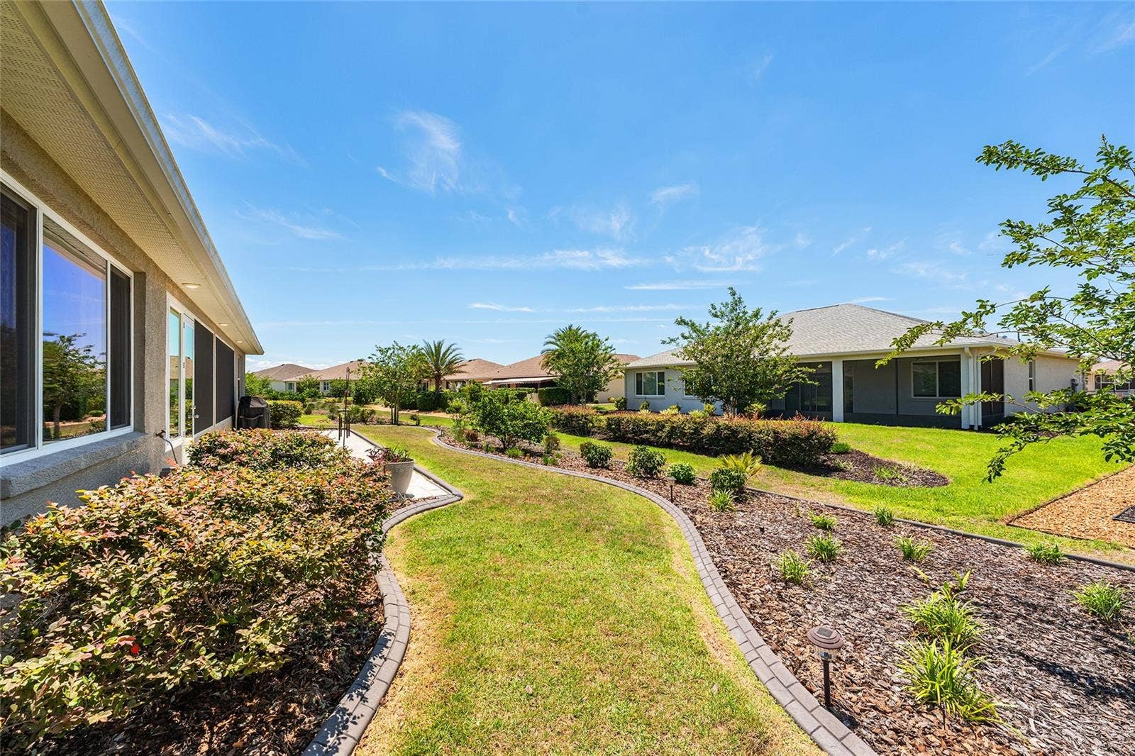 Beautifully landscaped backyard featuring attractive concrete curbing, established shrubs, colorful plantings, and a lush green lawn. Thoughtfully designed landscape beds enhance the outdoor setting and create an inviting space to enjoy Florida living.