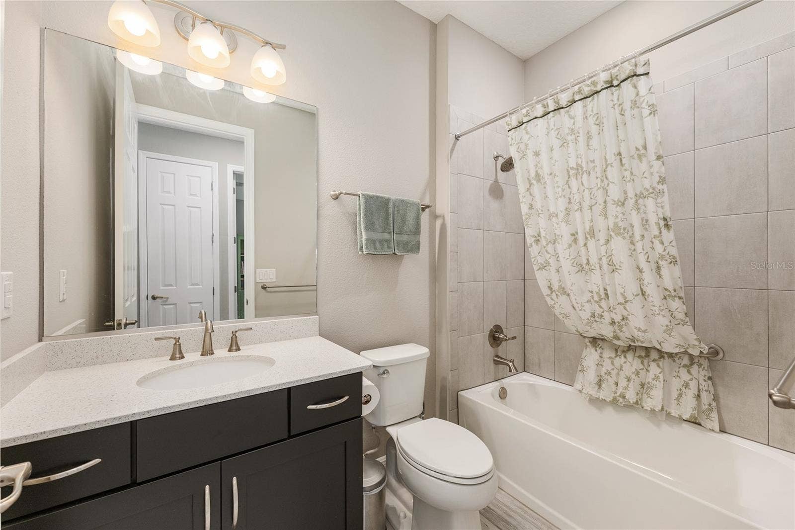 Conveniently located near the third bedroom, this guest bathroom features a spacious vanity with contrasting dark cabinetry, a large mirror, and a tiled tub/shower combination.