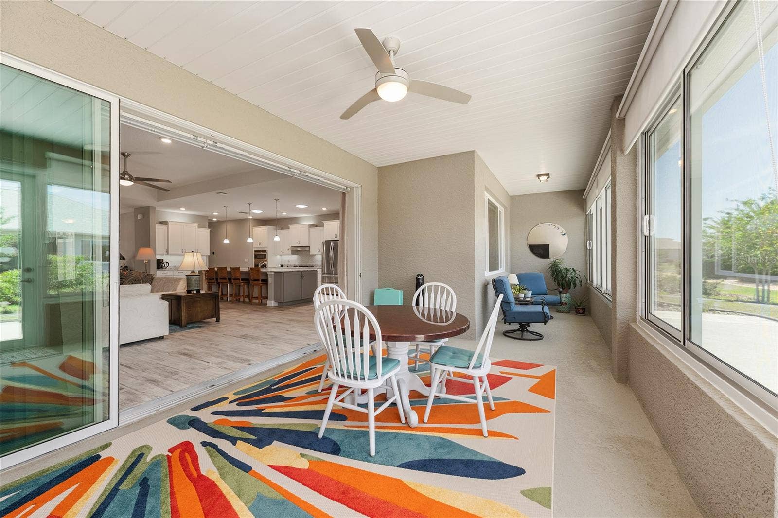 Inviting enclosed lanai featuring a seamless, zero-entry transition from the great room, finished walls, a 24-inch knee wall, ceiling fan with integrated lighting, convenient GFCI outlet, and custom solar shades for added comfort and privacy.