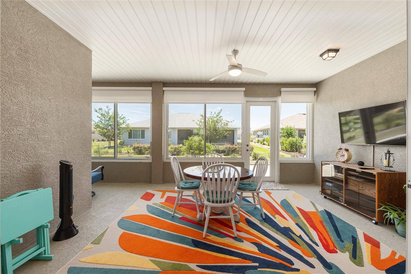 Inviting enclosed lanai featuring custom solar shades, a ceiling fan with integrated lighting, and expansive windows that fill the space with natural light. A perfect setting for relaxing or entertaining, with the wall-mounted TV included in the sale.