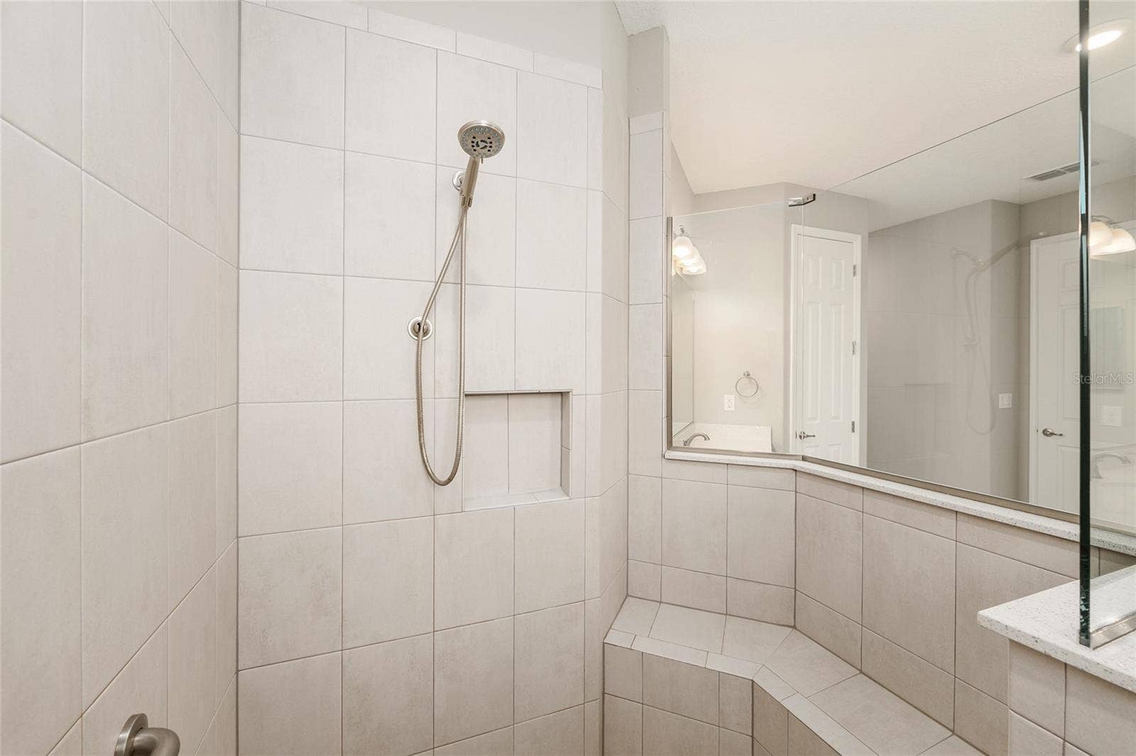 Closer view of the first primary suite's beautifully tiled shower, showcasing the integrated corner bench and thoughtfully designed space for added comfort and convenience.