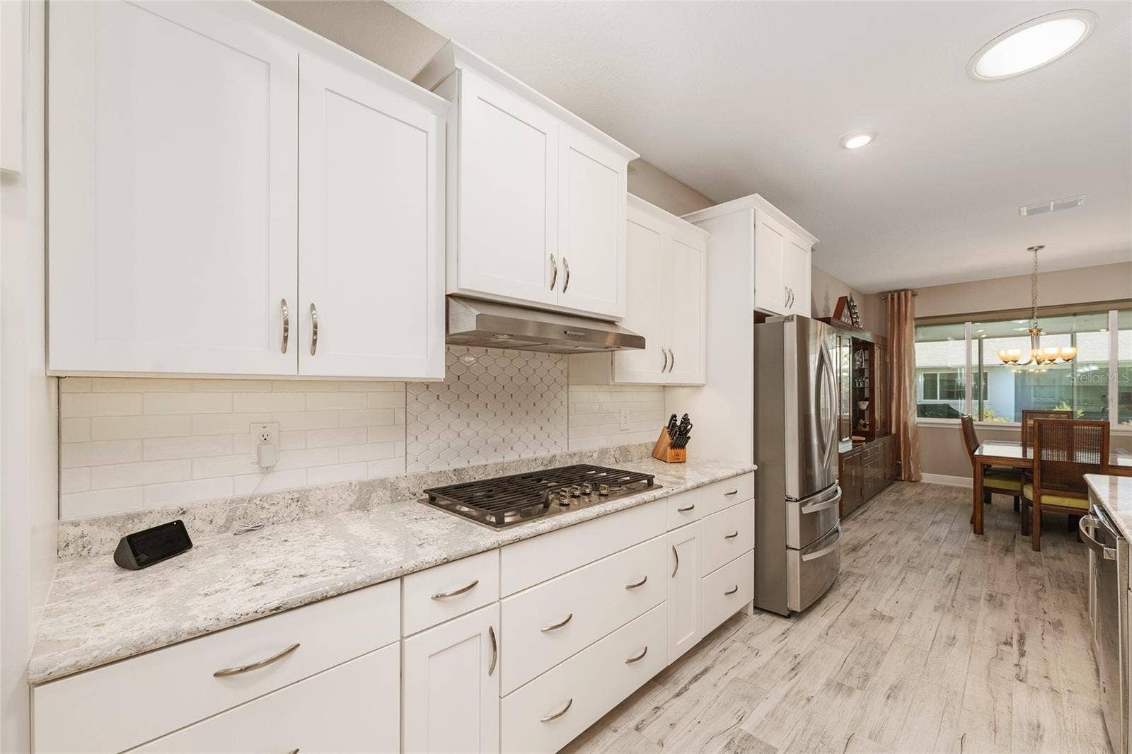 Well-appointed kitchen featuring abundant pot drawers, stainless steel appliances, a GE five-burner gas cooktop, neutral tile backsplash, Cambria quartz countertops, and an open flow into the dining area.