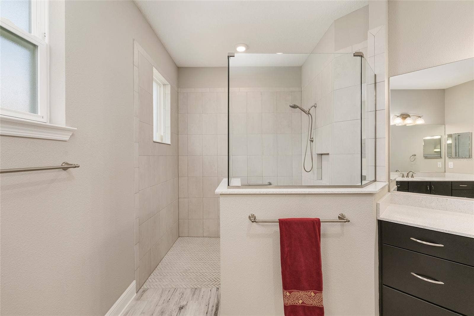 Spacious first primary ensuite bathroom featuring a large zero-entry walk-in shower with glass enclosure, tile surround, built-in niche, handheld shower fixture, and a bright, open design for everyday comfort and convenience.