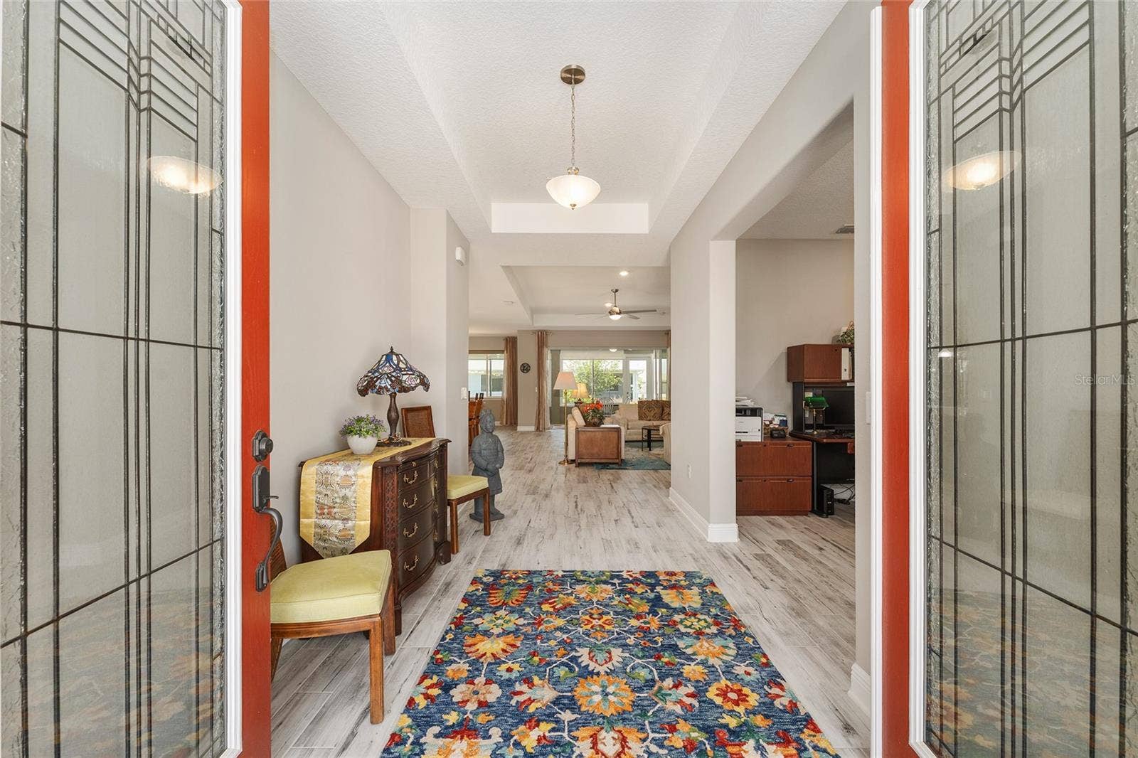 Inviting foyer featuring elegant leaded-glass double entry doors, a decorative tray ceiling, and ceramic plank flooring, creating a bright and welcoming introduction to the home.