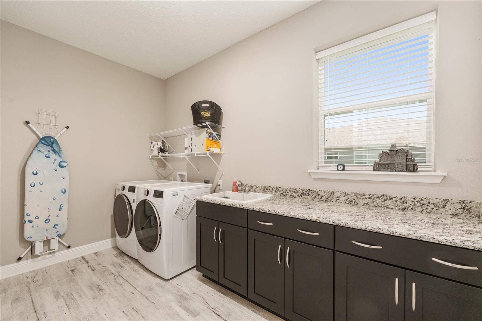 Spacious laundry room featuring abundant cabinetry, expansive granite countertops, a convenient utility sink, and a window providing natural light. Includes an LG front-load washer and gas dryer, with an additional electric dryer connection for flexibility.