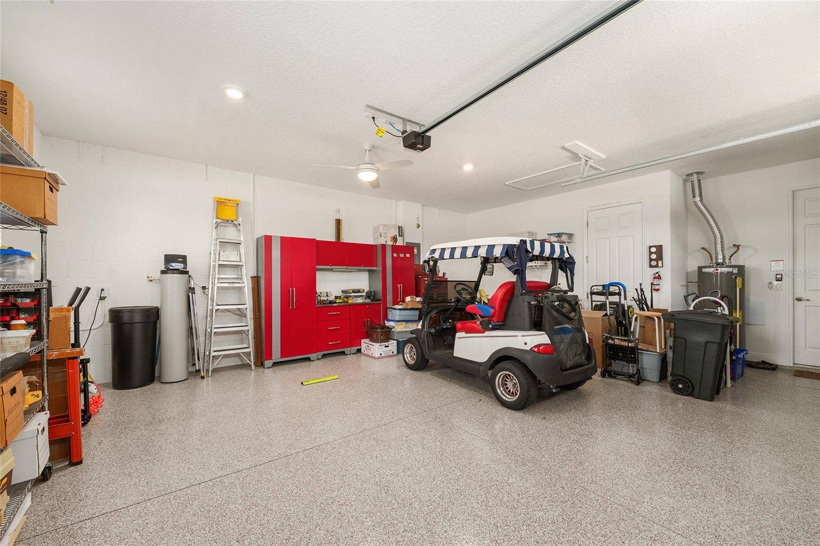Spacious two-car garage featuring durable epoxy flooring, an insulated garage door with heavy-duty springs, recessed lighting, a ceiling fan with integrated lighting, a convenient utility sink, and additional electrical outlets throughout. Plenty of room for parking, storage, and projects.