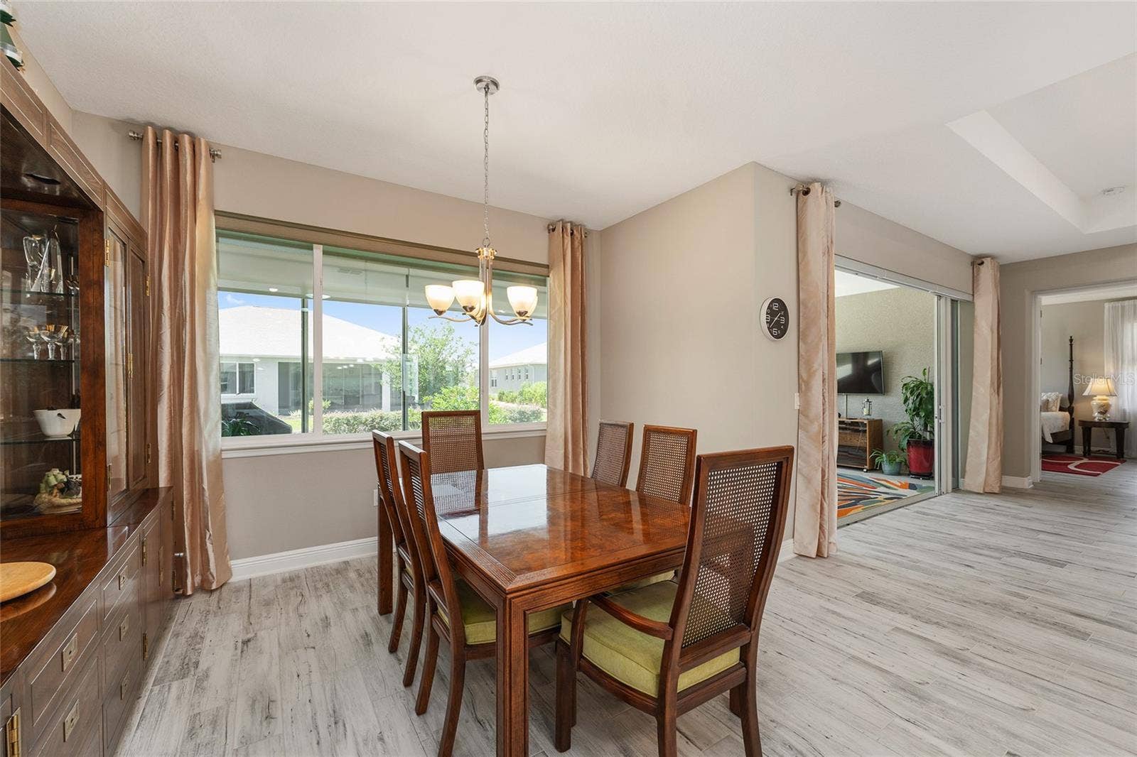 Bright and inviting dining area featuring large windows that fill the space with natural light, ceramic plank flooring, neutral finishes, and an open flow to the kitchen and great room, with convenient access to the enclosed lanai.