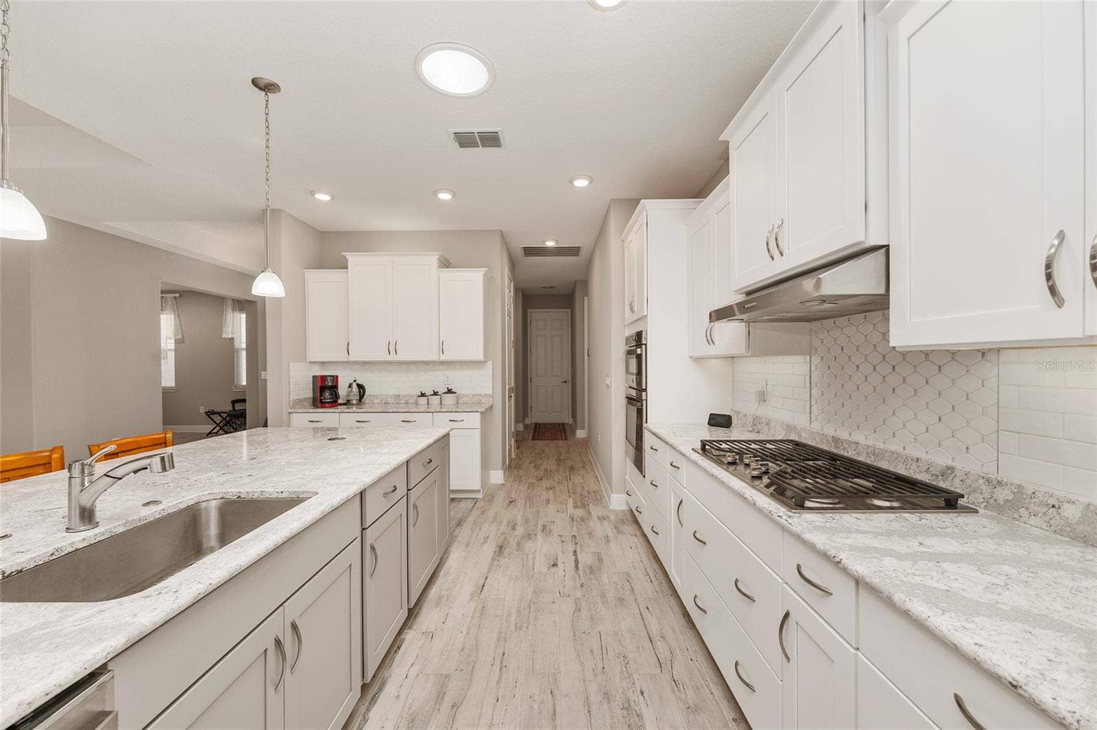 Beautifully designed kitchen featuring staggered cabinetry, Cambria quartz countertops, a decorative tile backsplash, GE five-burner gas cooktop, over- and under-cabinet lighting, switched outlets above the cabinets, ceramic plank flooring, recessed lighting, and an open layout connecting to the dining and great room.