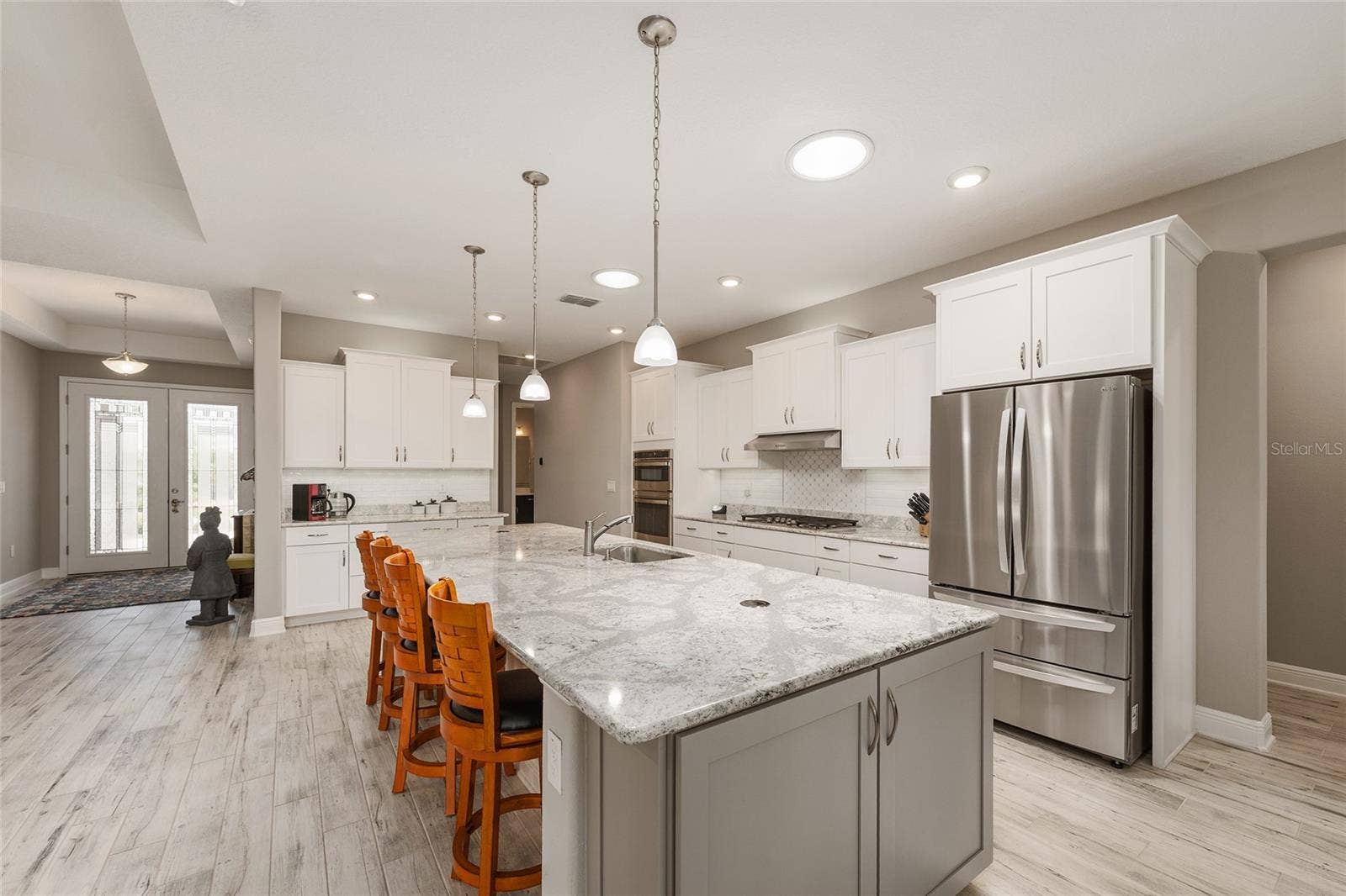 Beautifully appointed kitchen featuring staggered cabinetry, convenient pull-out drawers, a neutral tile backsplash, and two solar tubes that fill the space with natural light. GE gas range, GE dishwasher, and LG refrigerator complement the impressive 12' x 4.5' Cambria quartz island, complete with pop-up outlets and abundant additional storage.