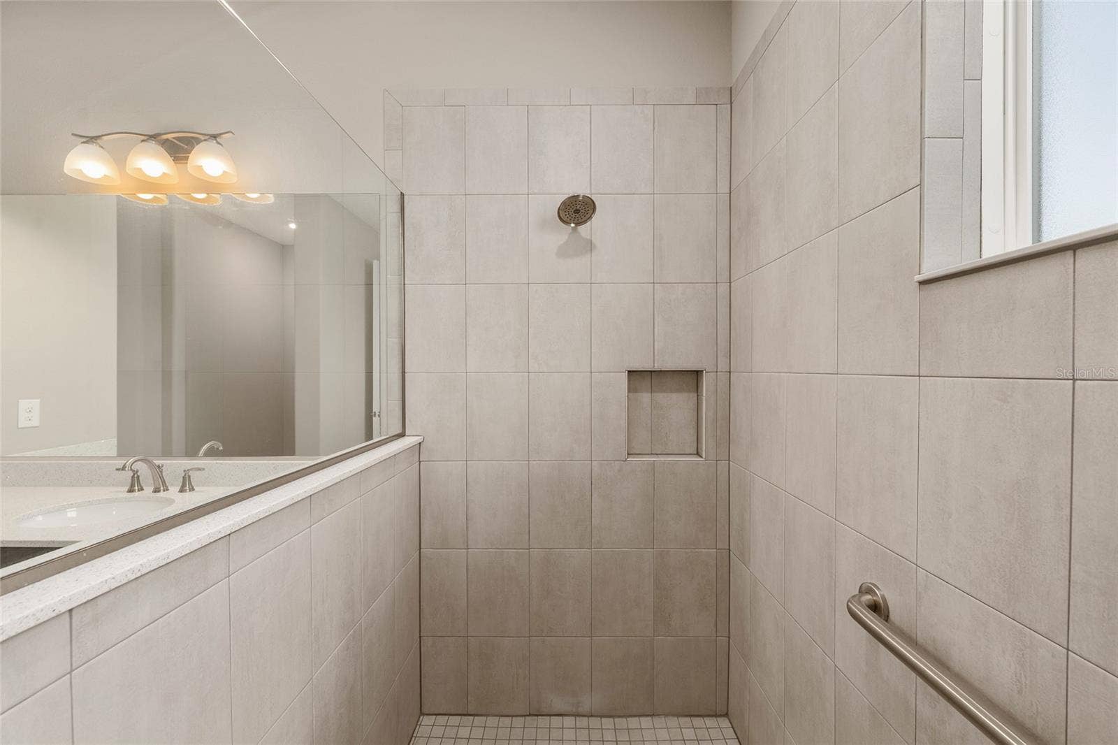 Closer view of the second primary ensuite shower, highlighting the built-in toiletry niche, conveniently positioned grab bar, and coordinating tile finishes for added functionality and comfort.