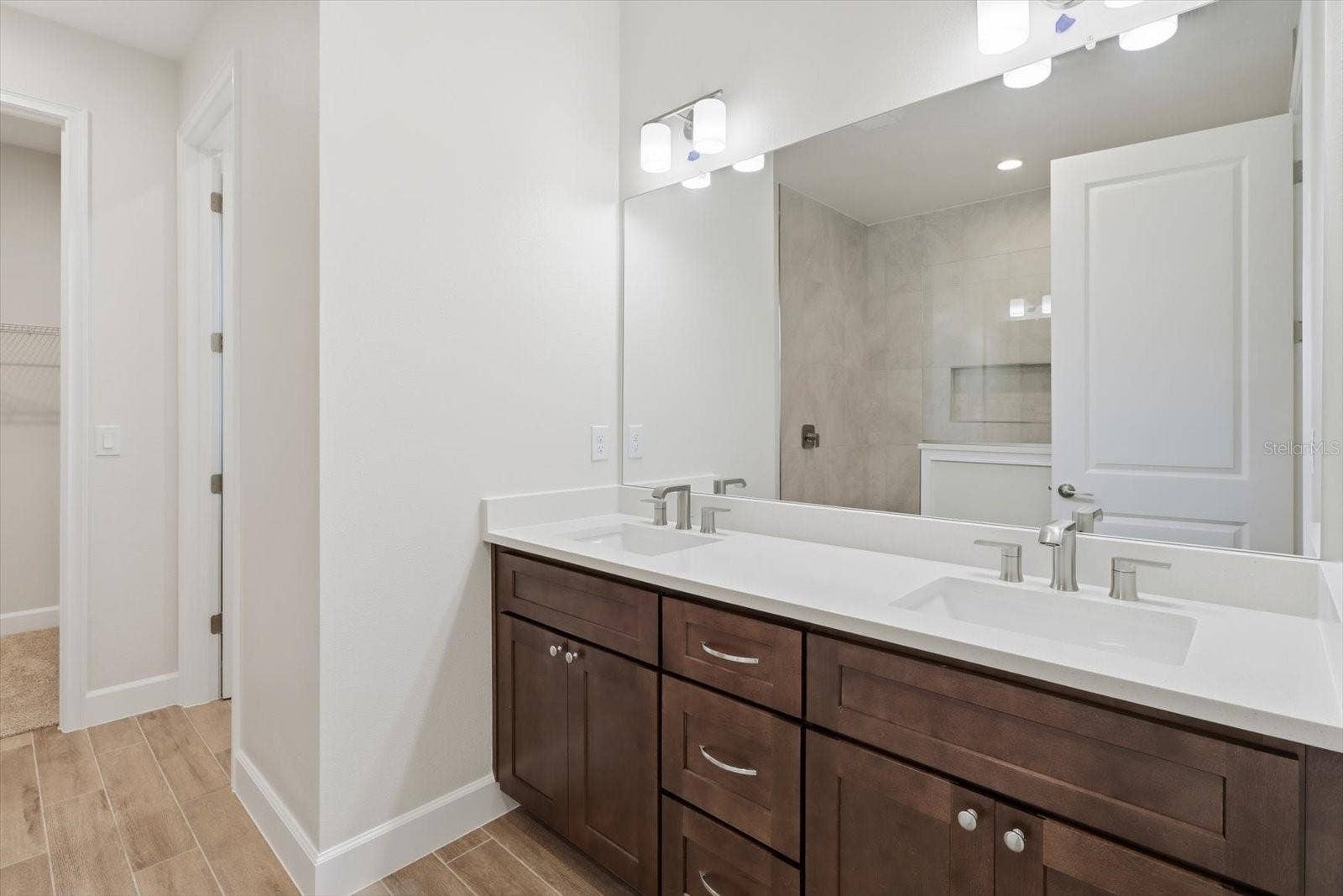 The primary bathroom has dual sinks, custom wood cabinets, and plank tile flooring.