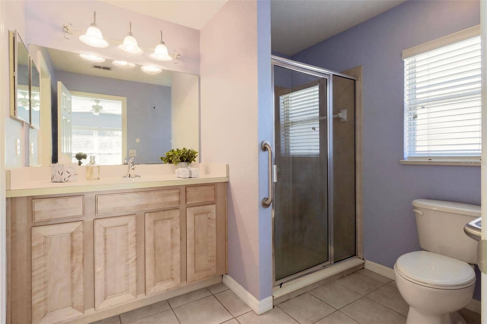 3437 GRENVILLE DRIVE, Winter Haven, FL 33884 The en-suite primary bathroom is designed for comfort, featuring a comfort-height vanity, tile flooring, and a walk-in shower with a glass door.