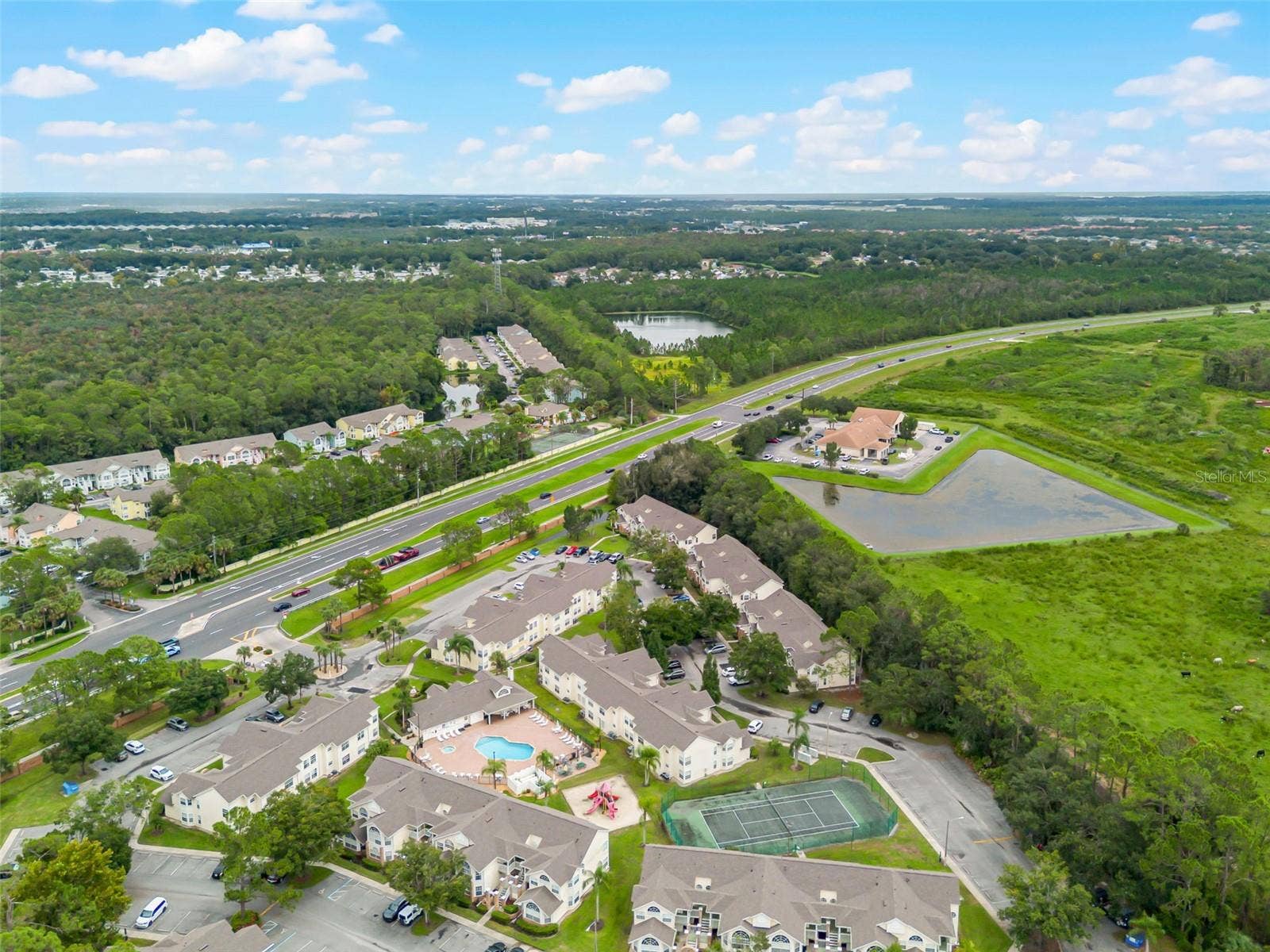 5017 LAGUNA BAY CIRCLE, #100, Kissimmee, FL 34746 Community & Highway Aerial: High-angle drone shot capturing the full neighborhood grounds, recreational amenities, retention ponds, and direct access to nearby thoroughfares.