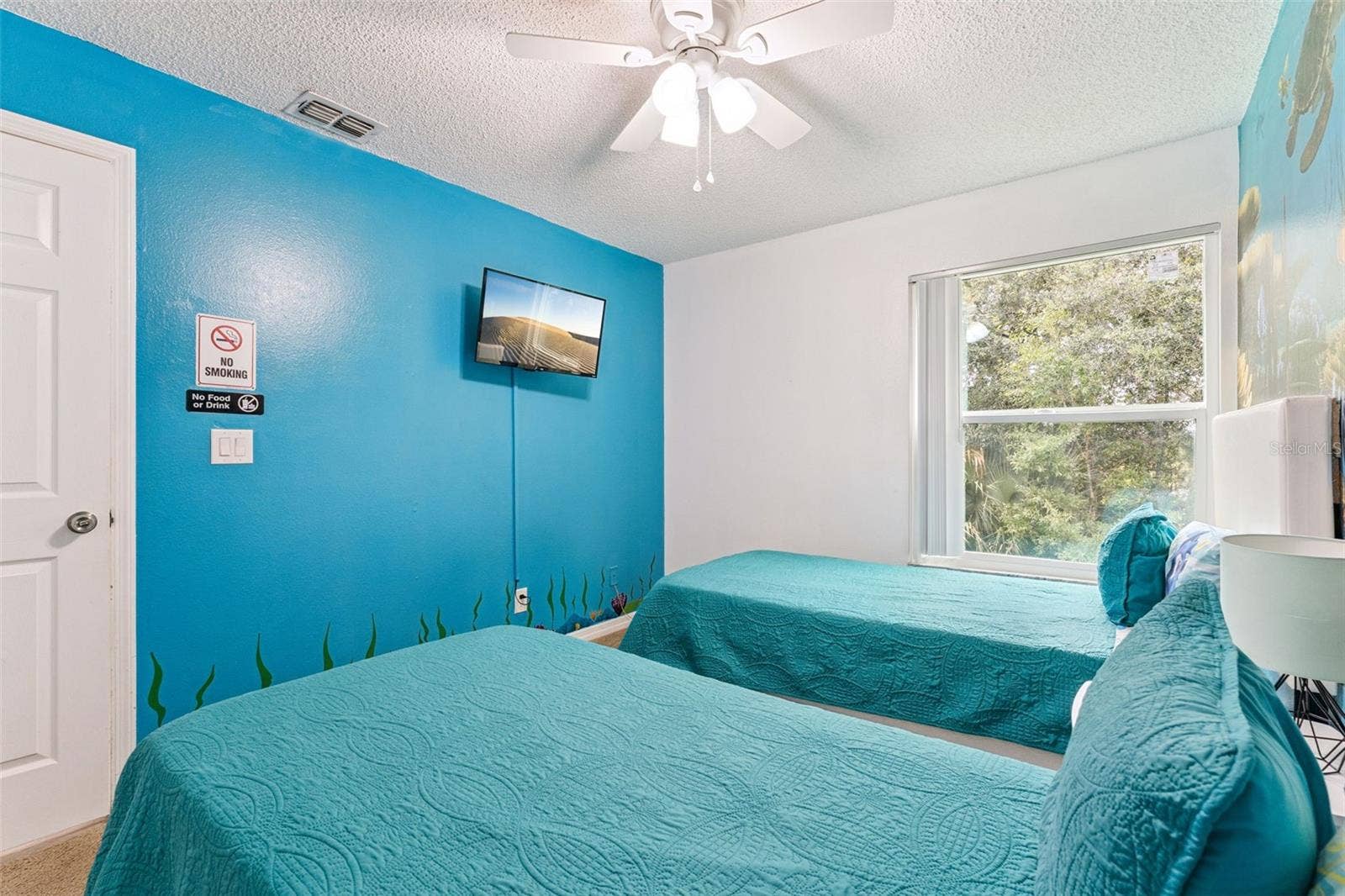 5017 LAGUNA BAY CIRCLE, #100, Kissimmee, FL 34746 Ocean-Themed Guest Bedroom: Bright guest bedroom featuring vibrant ocean blue accent walls, dual twin beds, a ceiling fan, and wall-mounted TV.