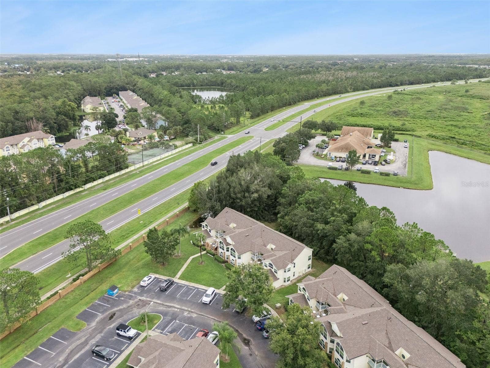 5017 LAGUNA BAY CIRCLE, #100, Kissimmee, FL 34746 Community Layout Aerial: Angled aerial perspective showcasing the residential building relative to nearby community amenities, water features, and main road