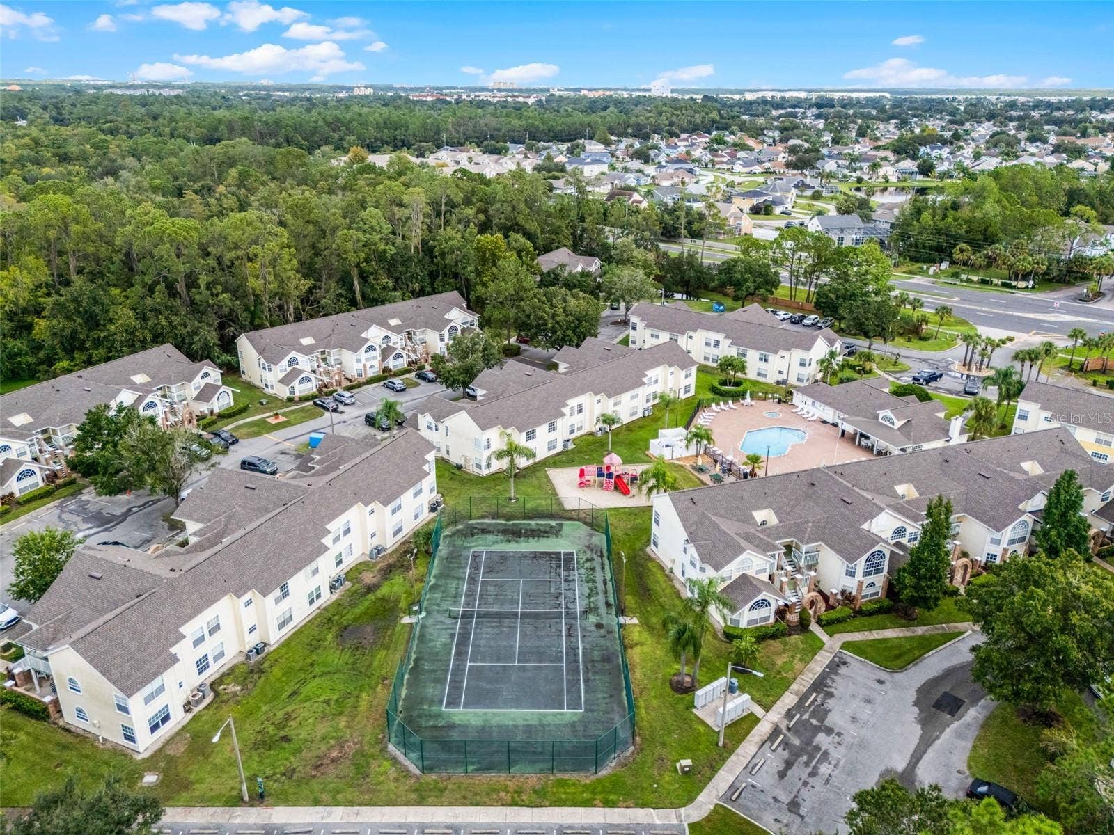 5017 LAGUNA BAY CIRCLE, #100, Kissimmee, FL 34746 Community Amenities Aerial: High-angle drone shot displaying key community features, including the fenced tennis court, children's playground, resort pool, clubhouse, and surrounding residential buildings.