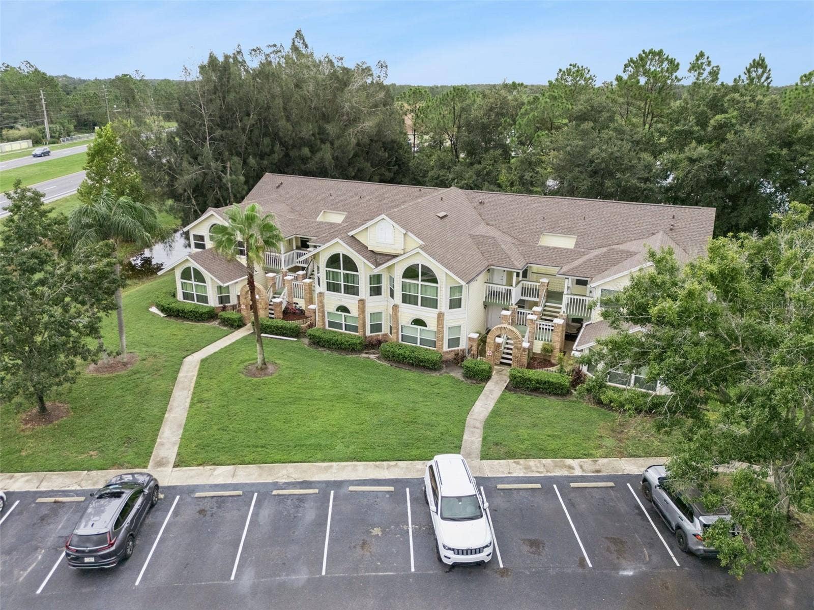5017 LAGUNA BAY CIRCLE, #100, Kissimmee, FL 34746 Building Facade Aerial: Focused front aerial capture highlighting the exterior facade, brick-accented entryways, central lawn, and parking access.
