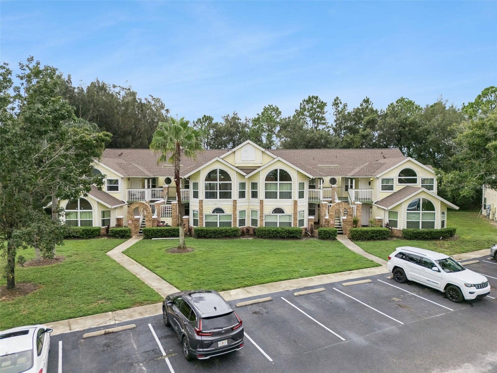 5017 LAGUNA BAY CIRCLE, #100, Kissimmee, FL 34746 Front Elevation View: Low-angle drone photo showcasing the full building exterior, grand architectural arched windows, entry staircases, and front parking lot.