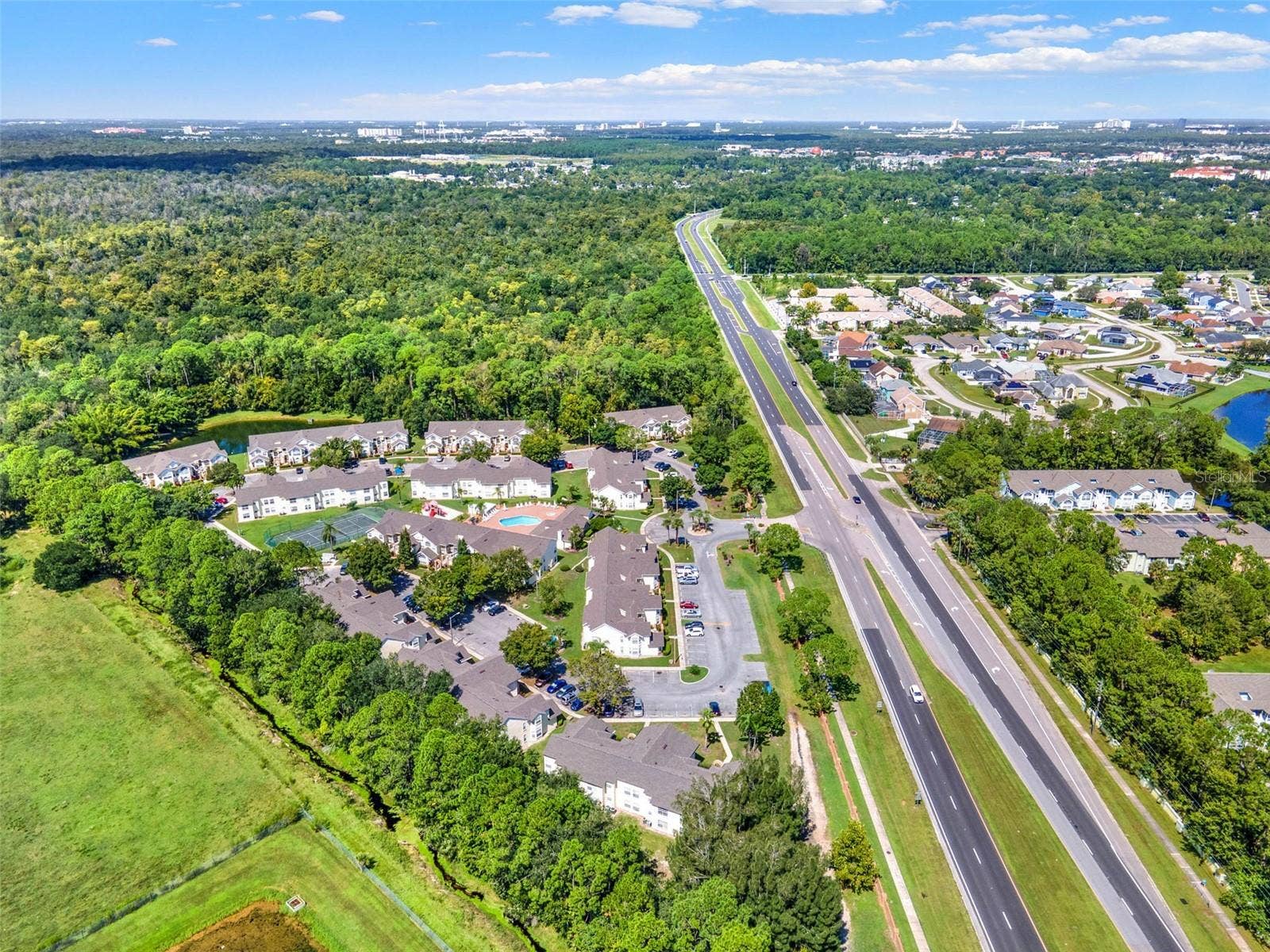 5017 LAGUNA BAY CIRCLE, #100, Kissimmee, FL 34746 Regional Overview Aerial: High-altitude aerial view showcasing the entire community grounds, surrounding lush foliage, adjacent pond, and convenient highway access.