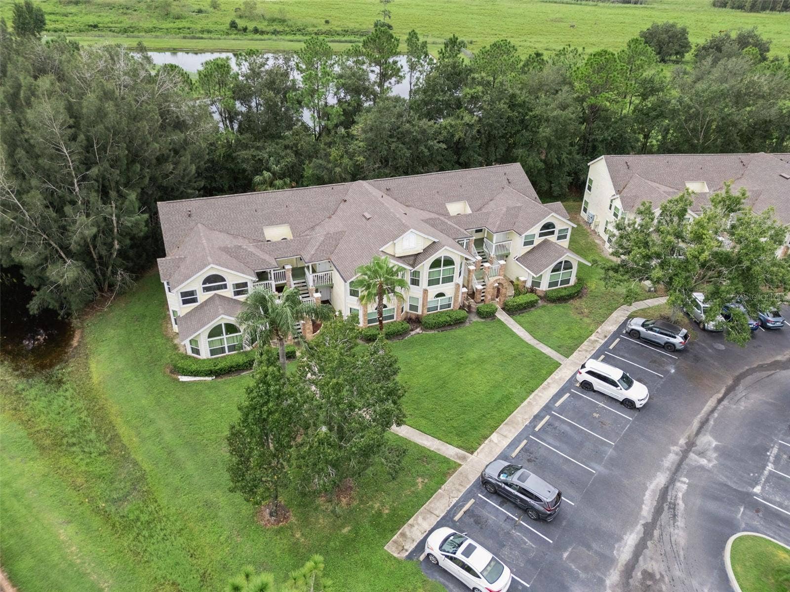 5017 LAGUNA BAY CIRCLE, #100, Kissimmee, FL 34746 Aerial Setting & Conservation View: High-angle aerial view showcasing the building tucked alongside a peaceful water feature and lush wooded backdrop