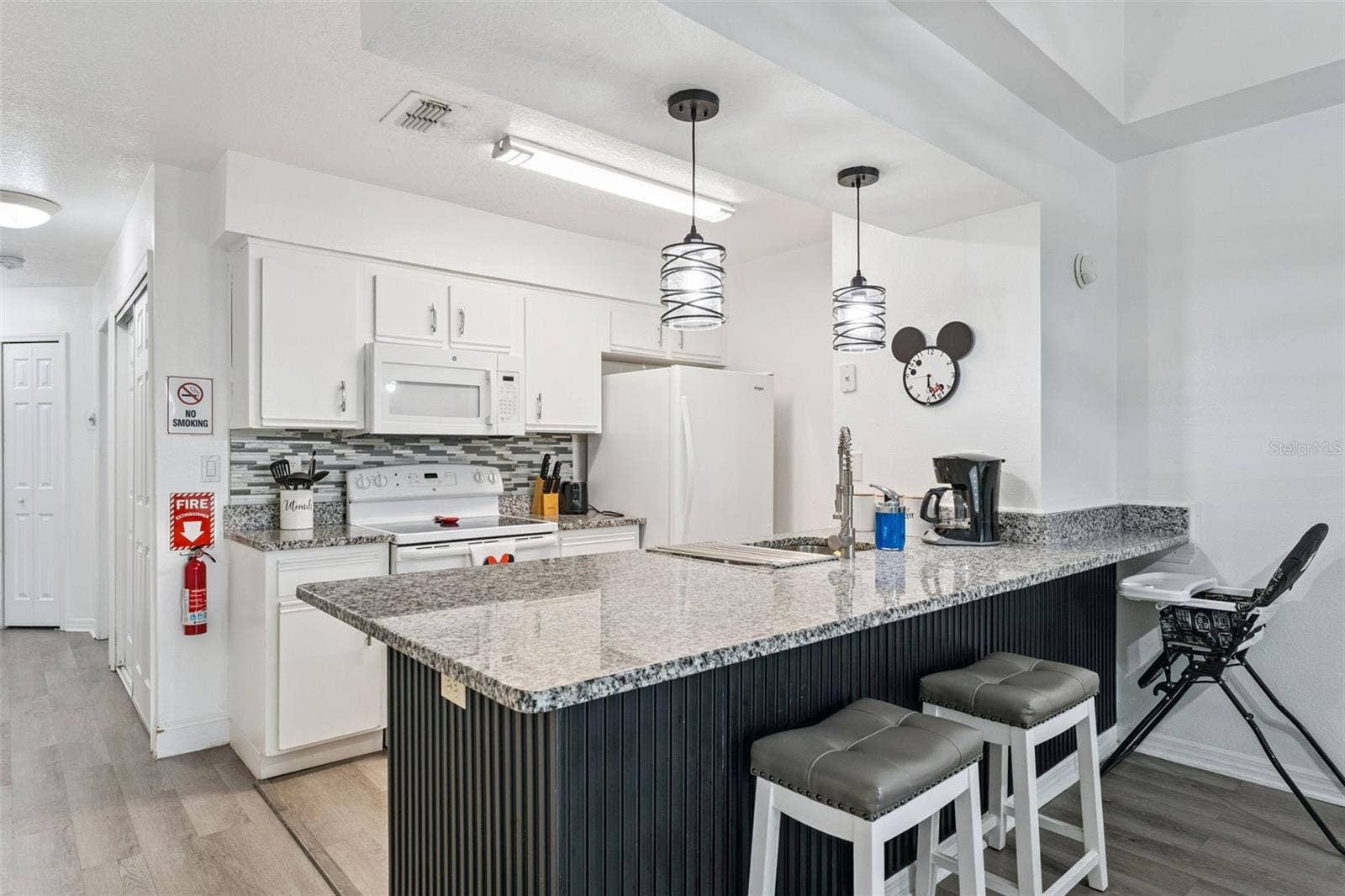 5017 LAGUNA BAY CIRCLE, #100, Kissimmee, FL 34746 Kitchen Island & Bar: Alternate angle of the kitchen peninsula bar with seating, rich dark wood-paneling detail, and view into the full kitchen suite.
