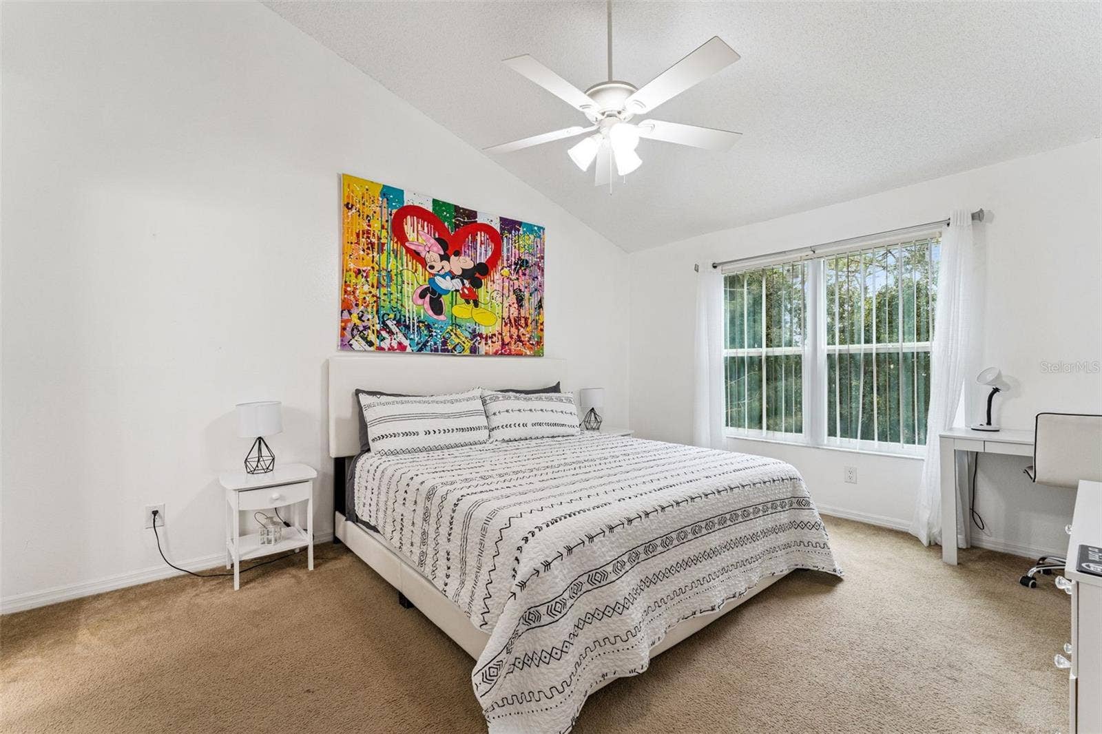 5017 LAGUNA BAY CIRCLE, #100, Kissimmee, FL 34746 Primary Suite Alternate Angle: Spacious primary suite showing room for a king bed, nightstands, decorative wall art, and cozy carpet flooring under high ceilings.