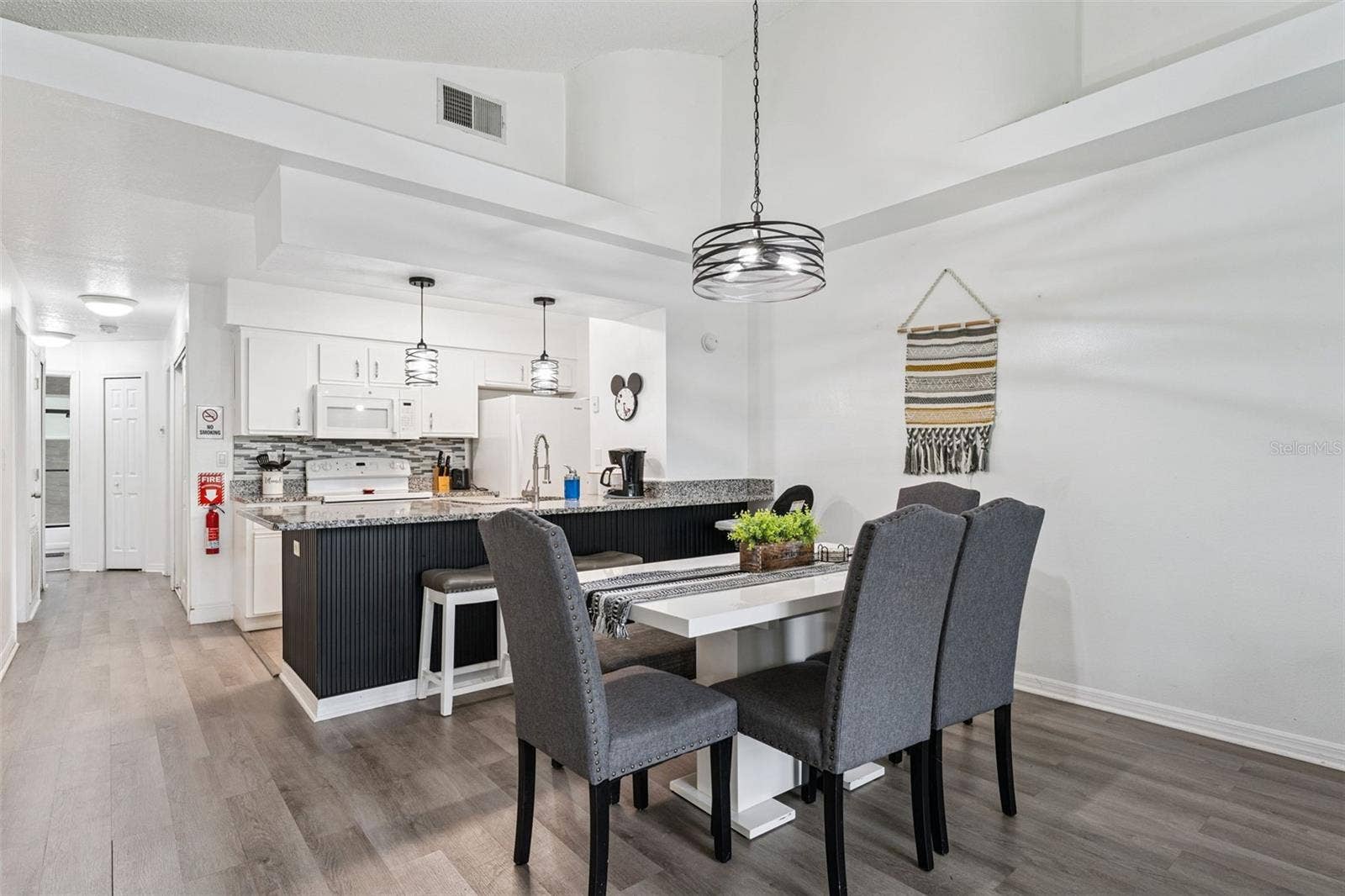 5017 LAGUNA BAY CIRCLE, #100, Kissimmee, FL 34746 Dining & Kitchen Flow: View of the dining area looking into the open kitchen, featuring high ceilings, modern pendant lighting, wood-look plank flooring, and a sleek breakfast bar.