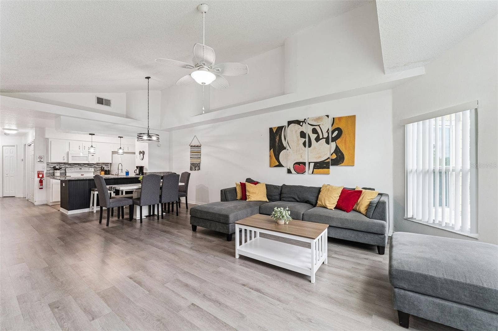 5017 LAGUNA BAY CIRCLE, #100, Kissimmee, FL 34746 Open-Concept Living & Dining: Open-plan main floor seamlessly connecting the spacious living area, dining space, and adjacent kitchen under vaulted ceilings.