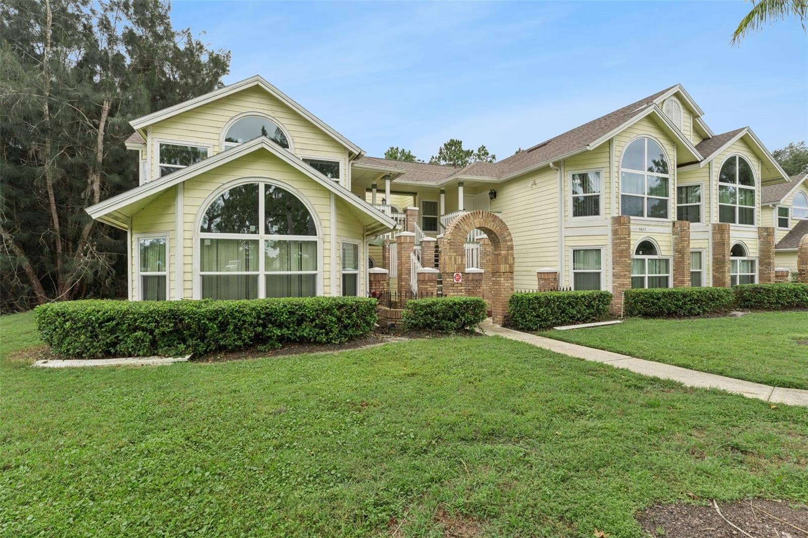 5017 LAGUNA BAY CIRCLE, #100, Kissimmee, FL 34746 Exterior Side View: Angled building view highlighting grand arched windows, brick accents, low-maintenance hedge landscaping, and lush lawn.